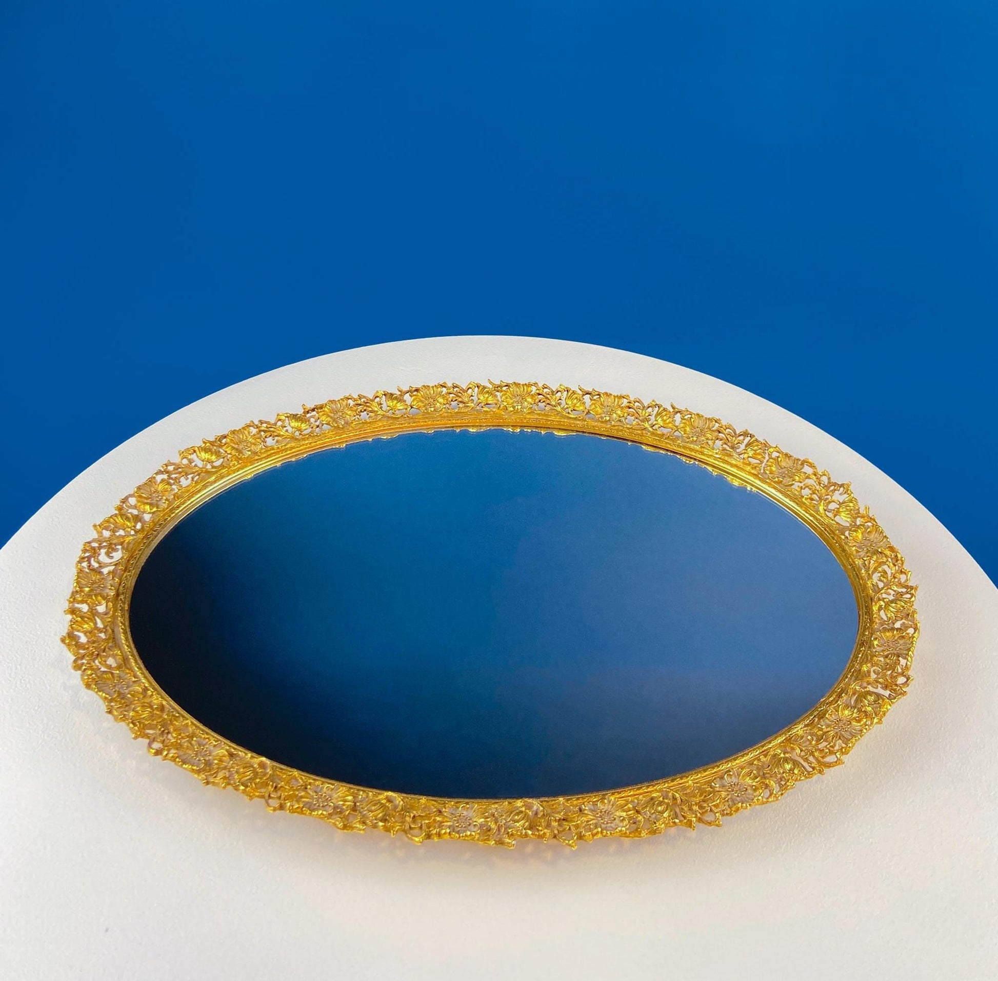 Decorative gold-framed mirror on a white base with a blue background