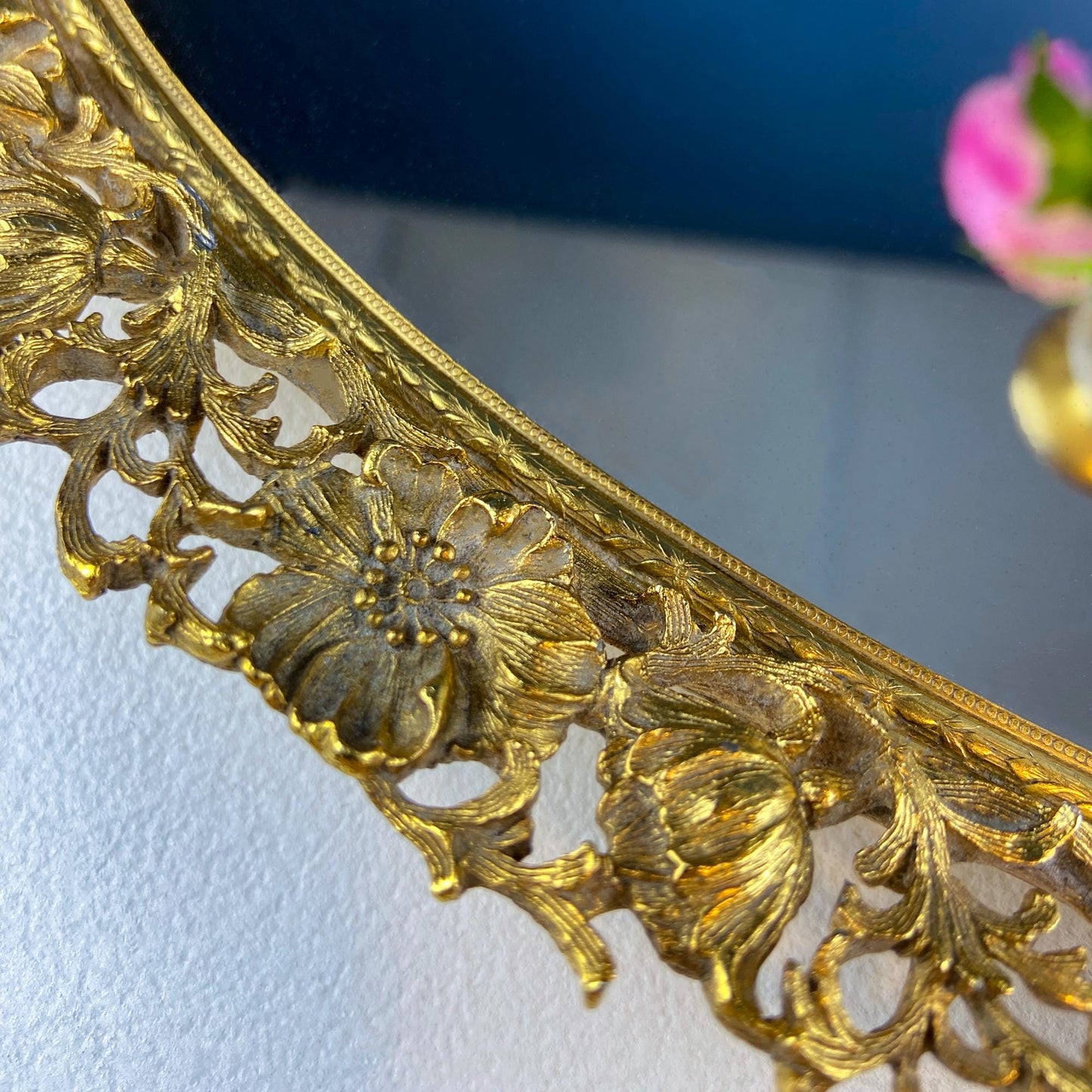 Close-up of a gold ornate mirror with floral designs on a white surface.