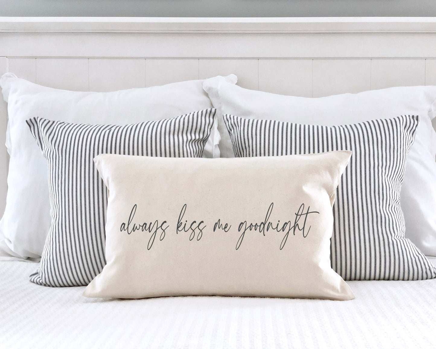 Always Kiss Me Goodnight Valentine's Day Pillow Cover 12x20 styled on a bed with striped pillows, perfect for Valentine's decor.
