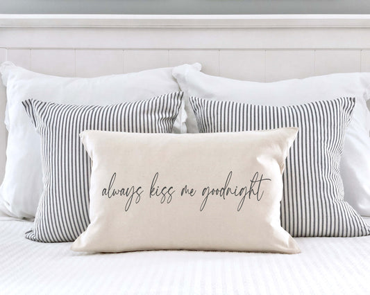 Always Kiss Me Goodnight Valentine's Day Pillow Cover 12x20 styled on a bed with striped pillows, perfect for Valentine's decor.