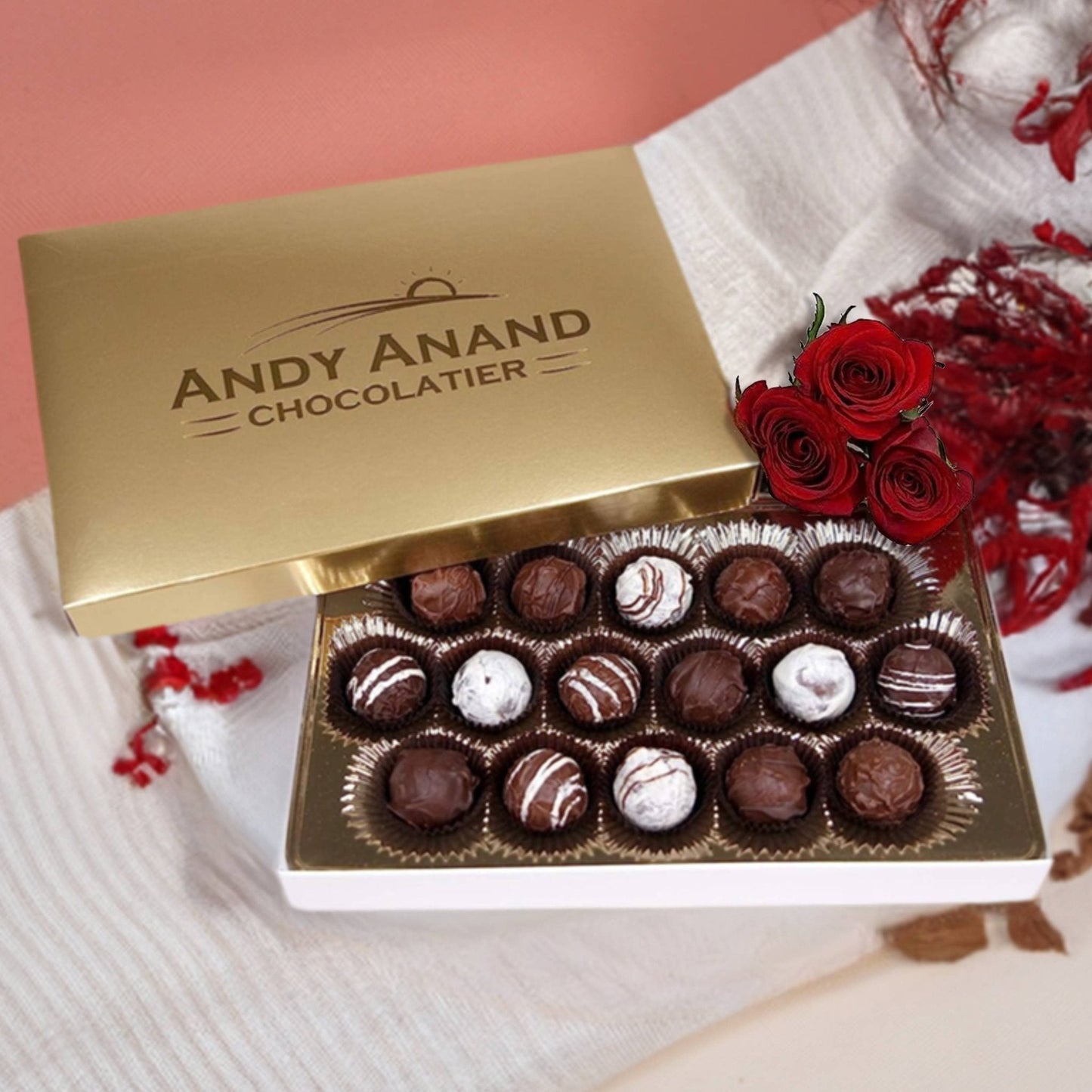Box of chocolates from Andy Anand Chocolatier with red roses on a pink background