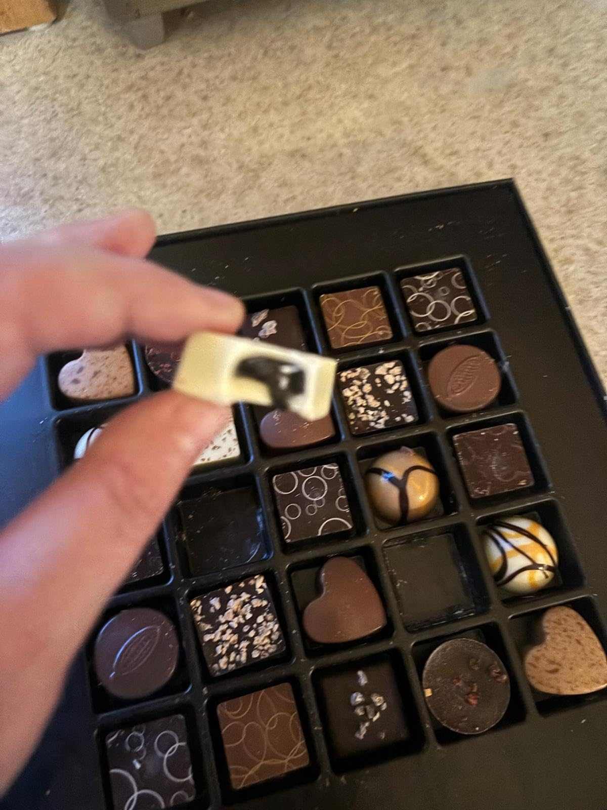 Assorted chocolates in a black box with a hand reaching for one.