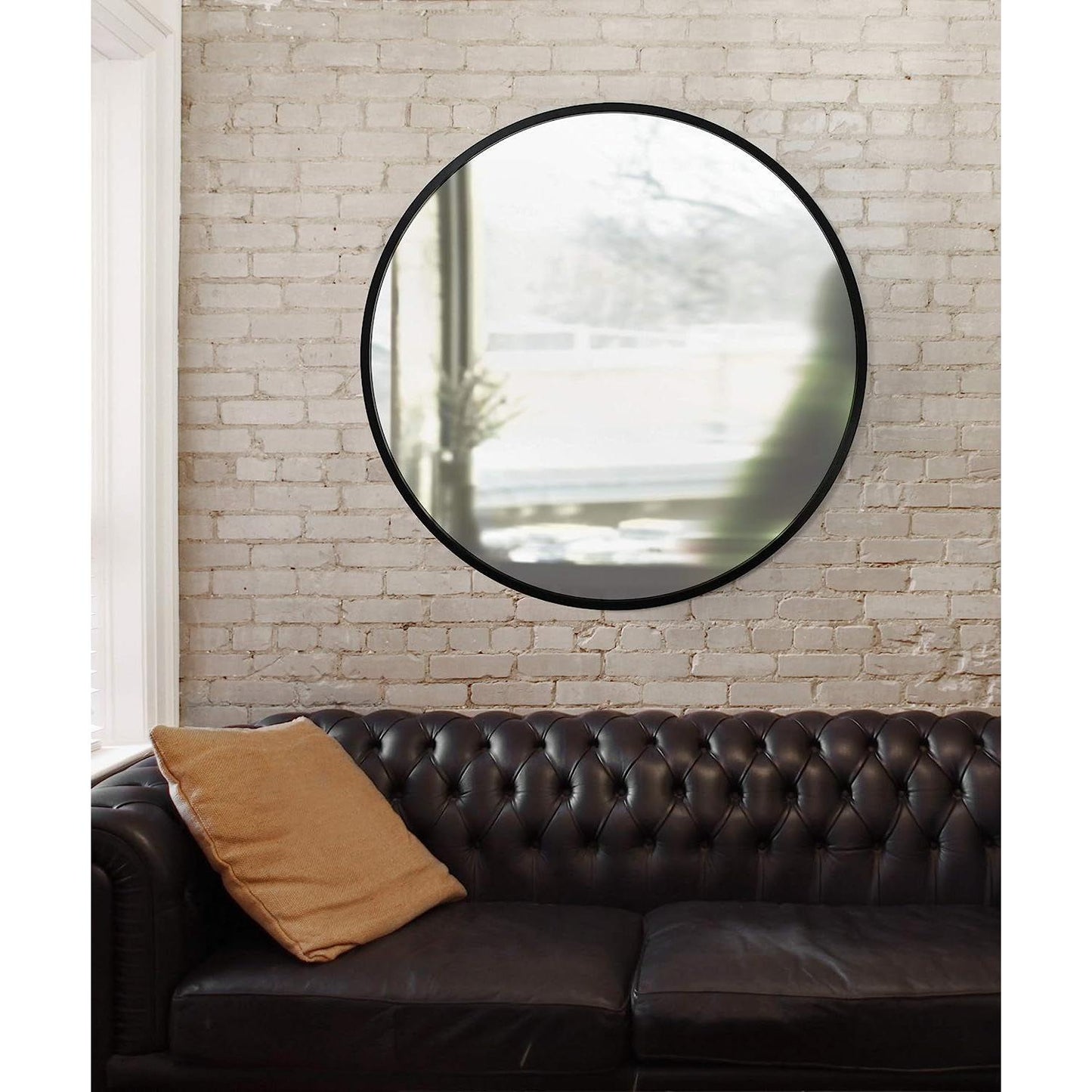 Round Rubber Wall Mirror 37 Inch diameter mounted on a white brick wall above a black leather couch.