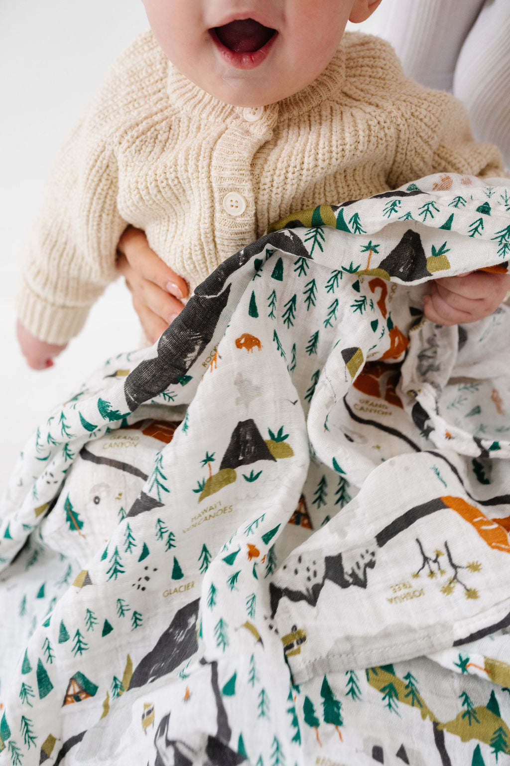 Baby holding a blanket with animal patterns on a white background