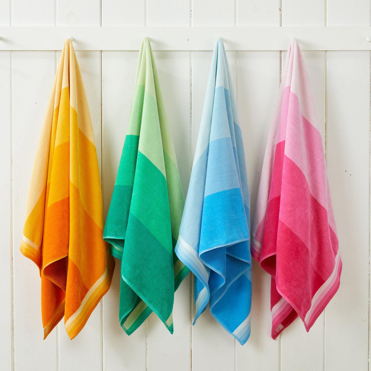 Four colorful beach towels hanging against a white wooden panel background.
