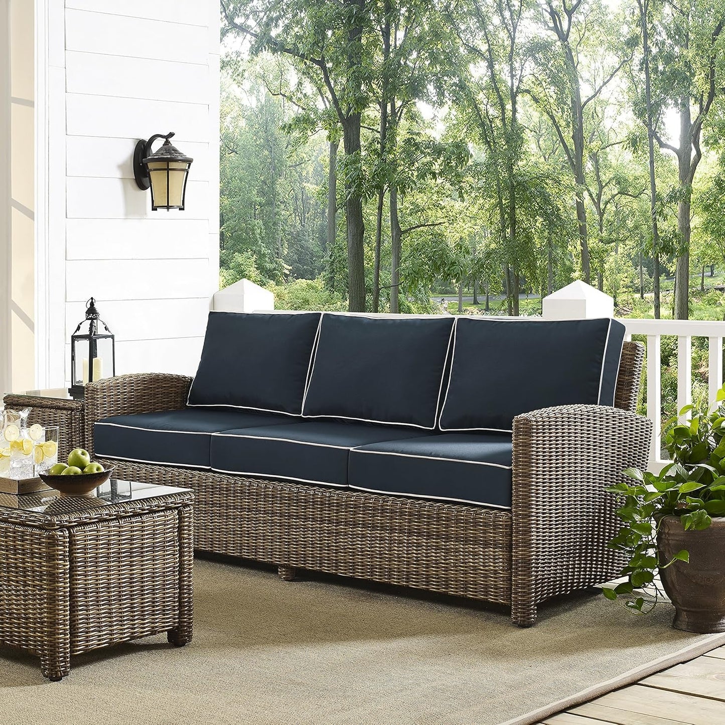 Brown Wicker Outdoor Sofa with Navy Cushions on a patio surrounded by greenery, perfect for outdoor relaxation.