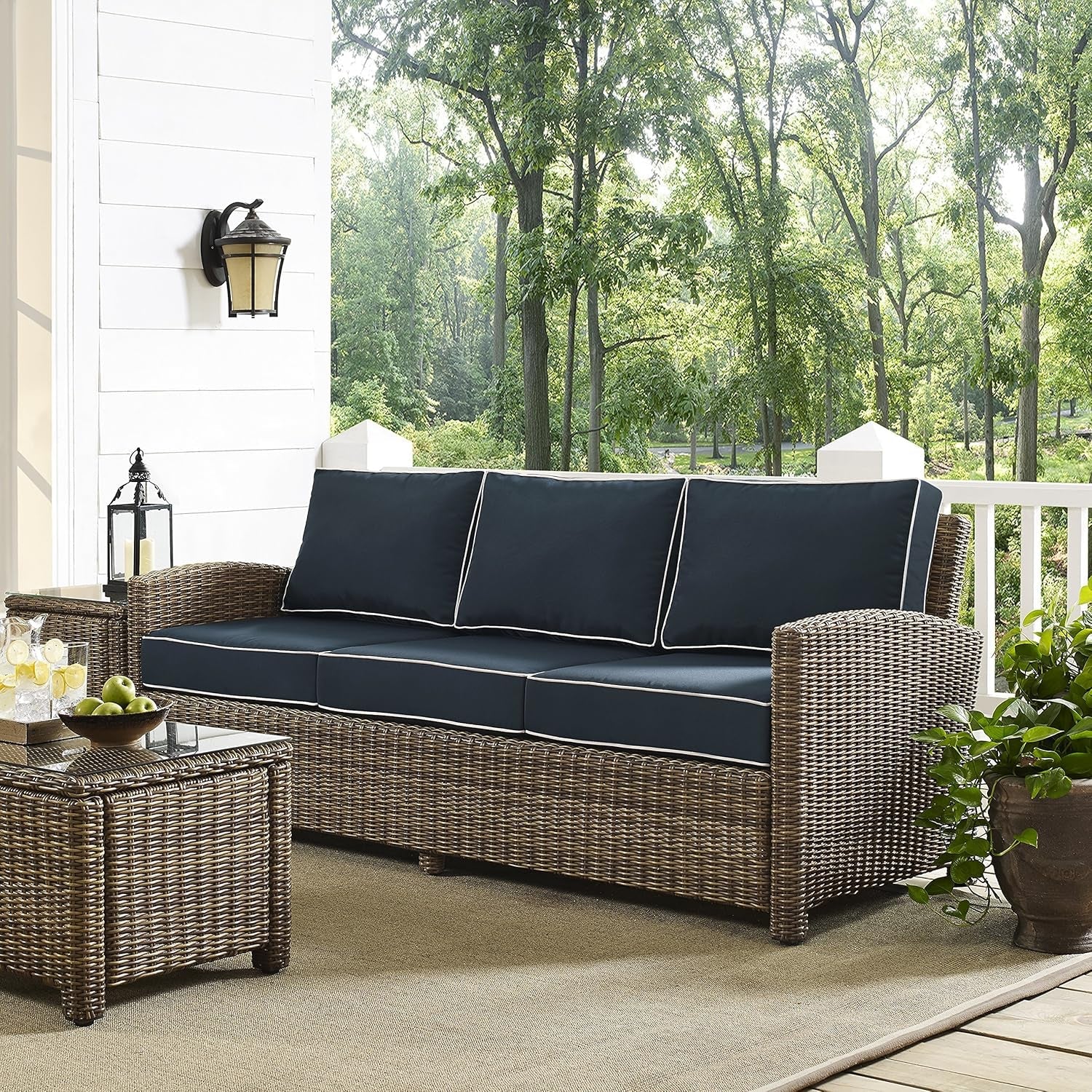 Brown Wicker Outdoor Sofa with Navy Cushions on a patio surrounded by greenery, perfect for outdoor relaxation.