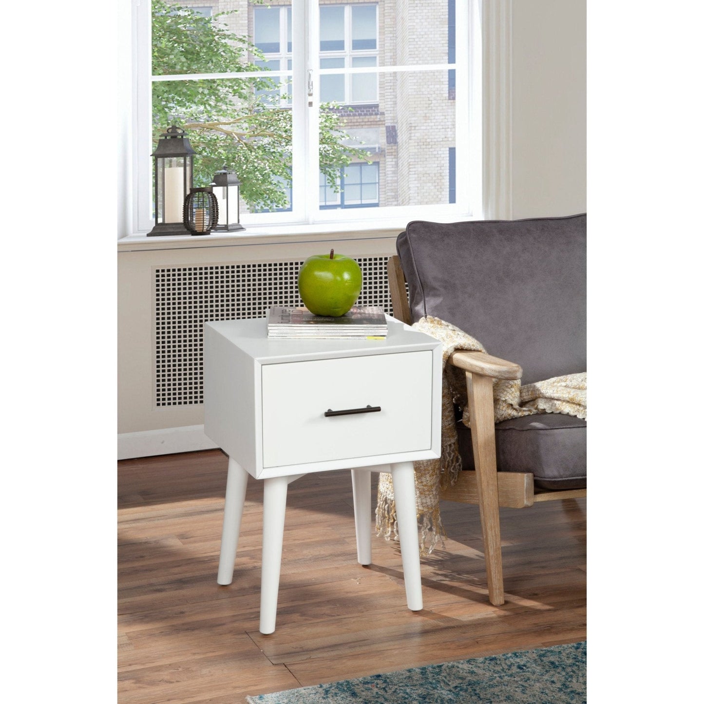 Flynn End Table in white with drawer beside a gray sofa and green apple on it, featuring sleek tapered legs and modern design.