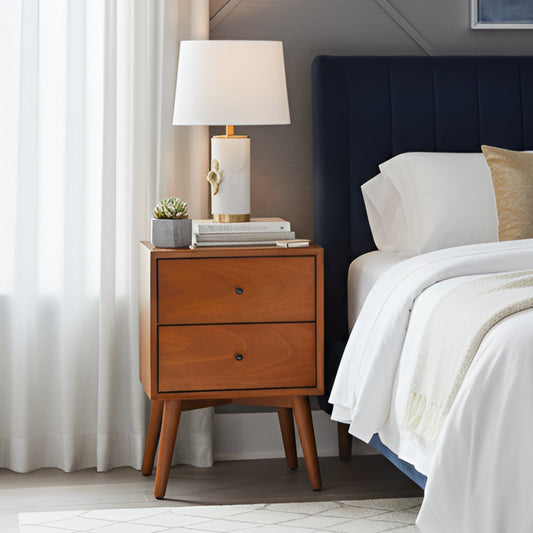Flynn Nightstand in chestnut finish with two drawers and lamp next to a bed in a modern bedroom setting.