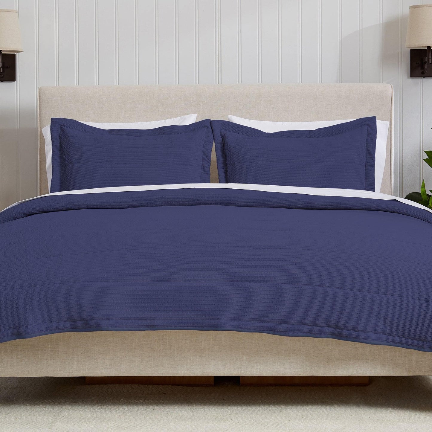 Navy blue bedding set on a bed with white pillows against a wooden panel wall.