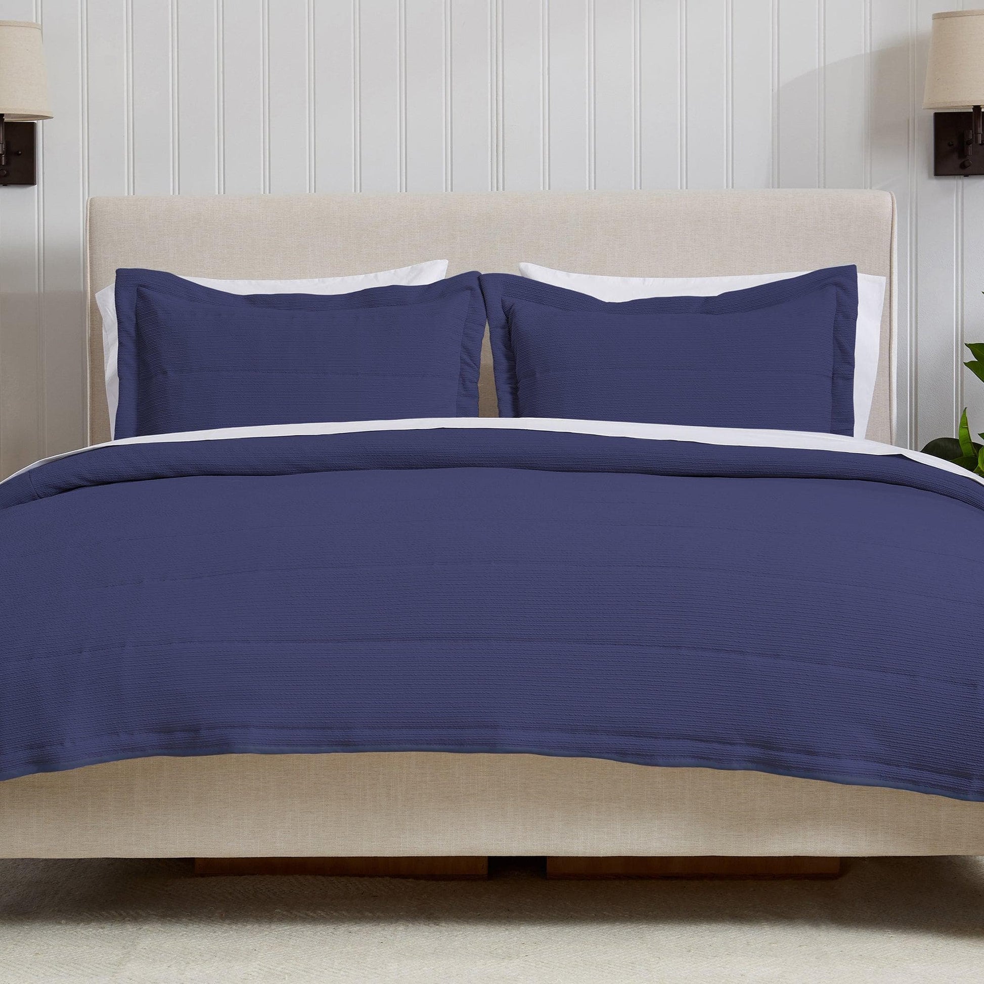 Navy blue bedding set on a bed with white pillows against a wooden panel wall.