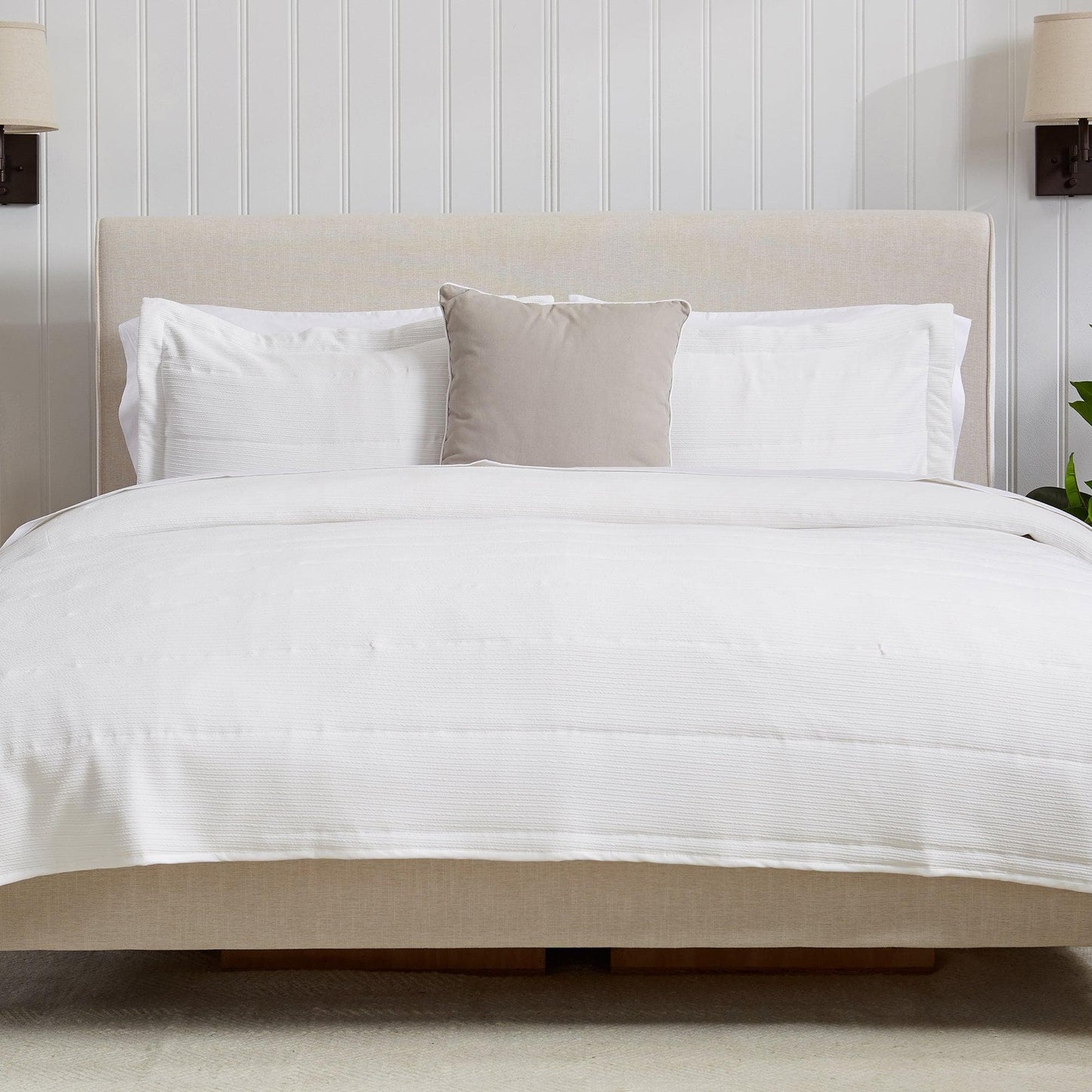 Neatly made bed with white bedding and pillows against a light-colored wall.