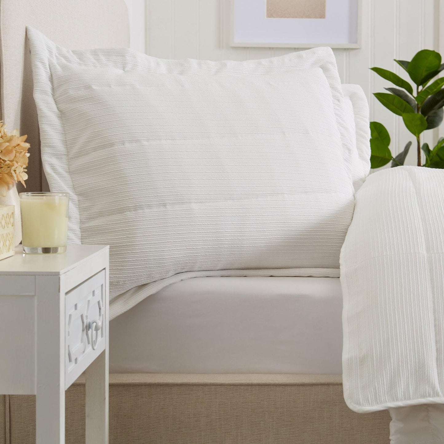 White bedding set on a bed with a side table and plant in the background