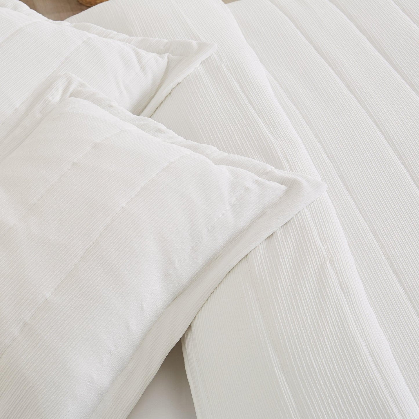 Close-up of white textured bedding with pillows on a light wooden surface