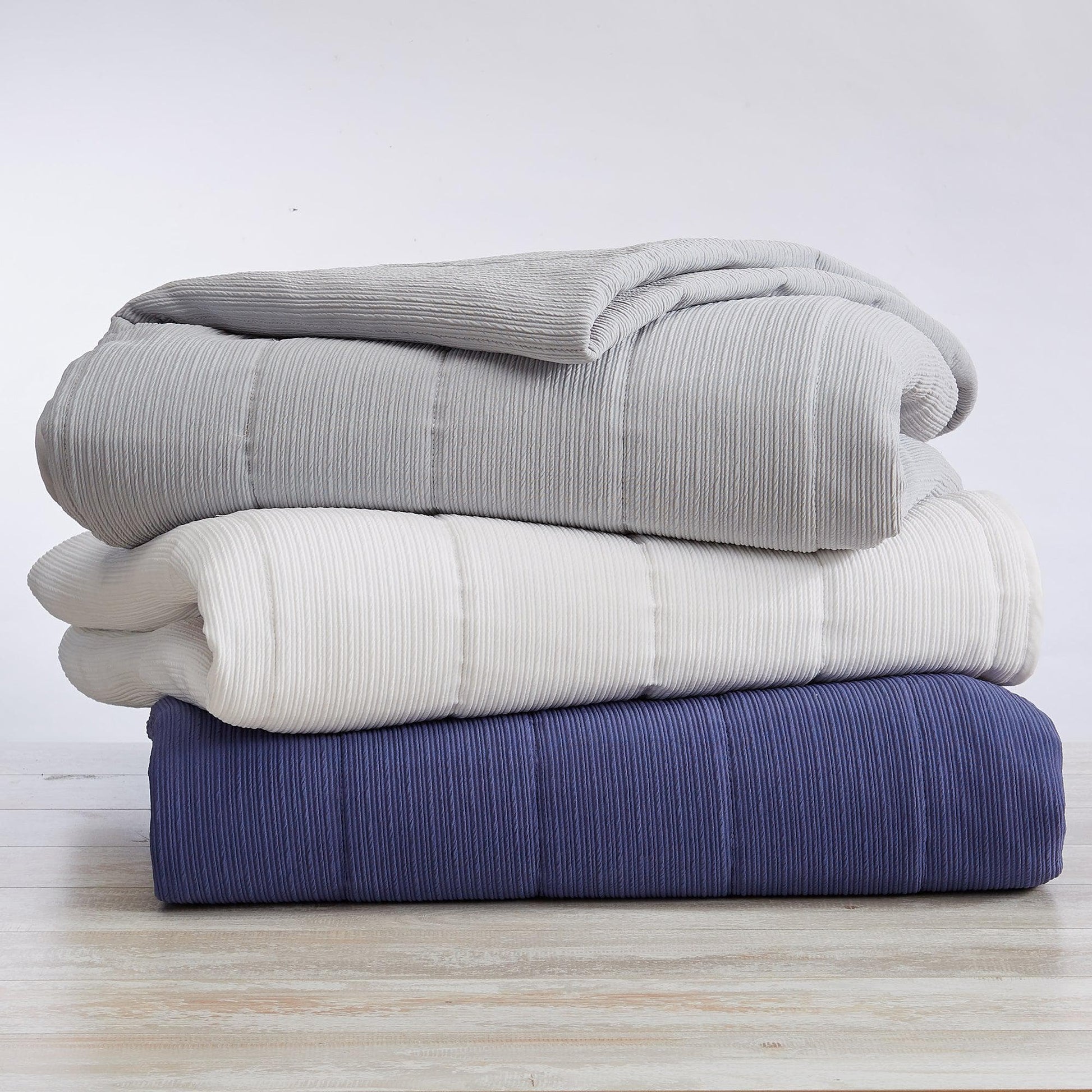 Stack of three folded blankets in gray, white, and blue on a light wooden surface.