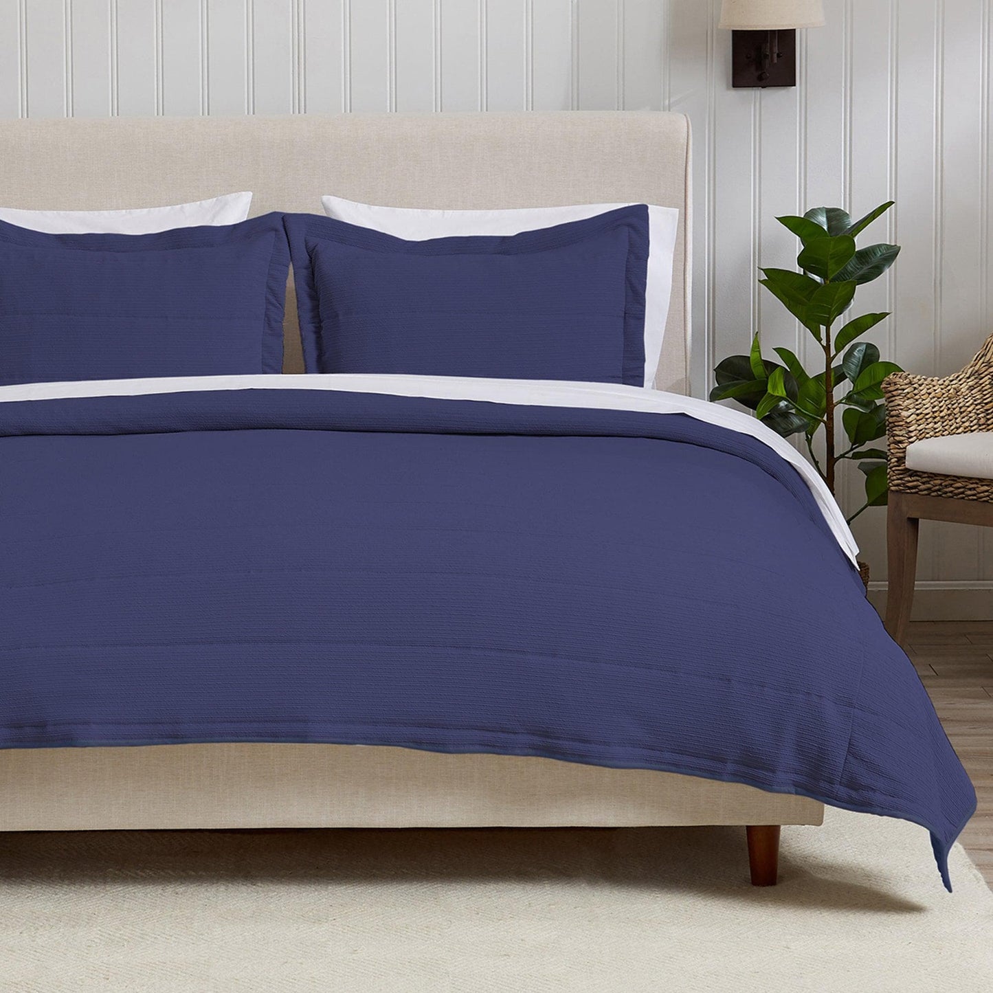 Navy blue bedding set on a bed in a bedroom with a plant and chair in the background.