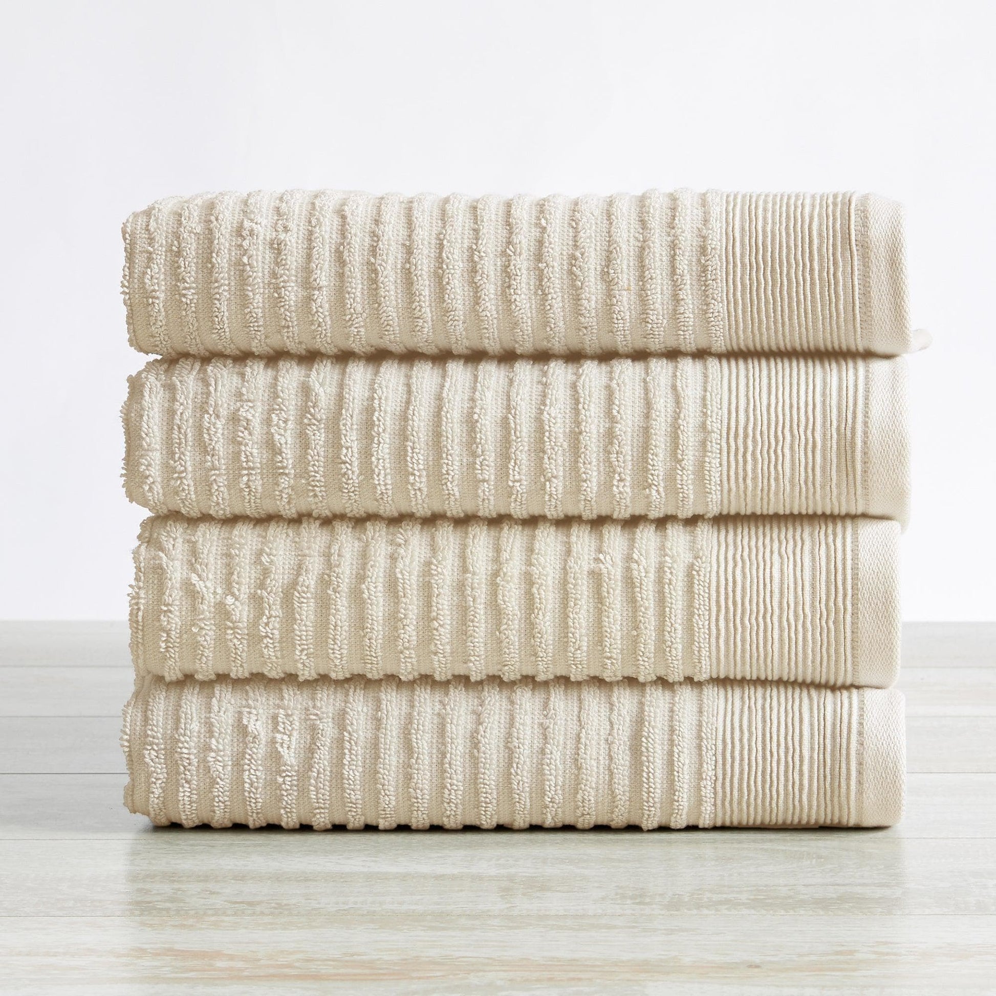 Stack of beige textured towels on a light wooden surface with a white background