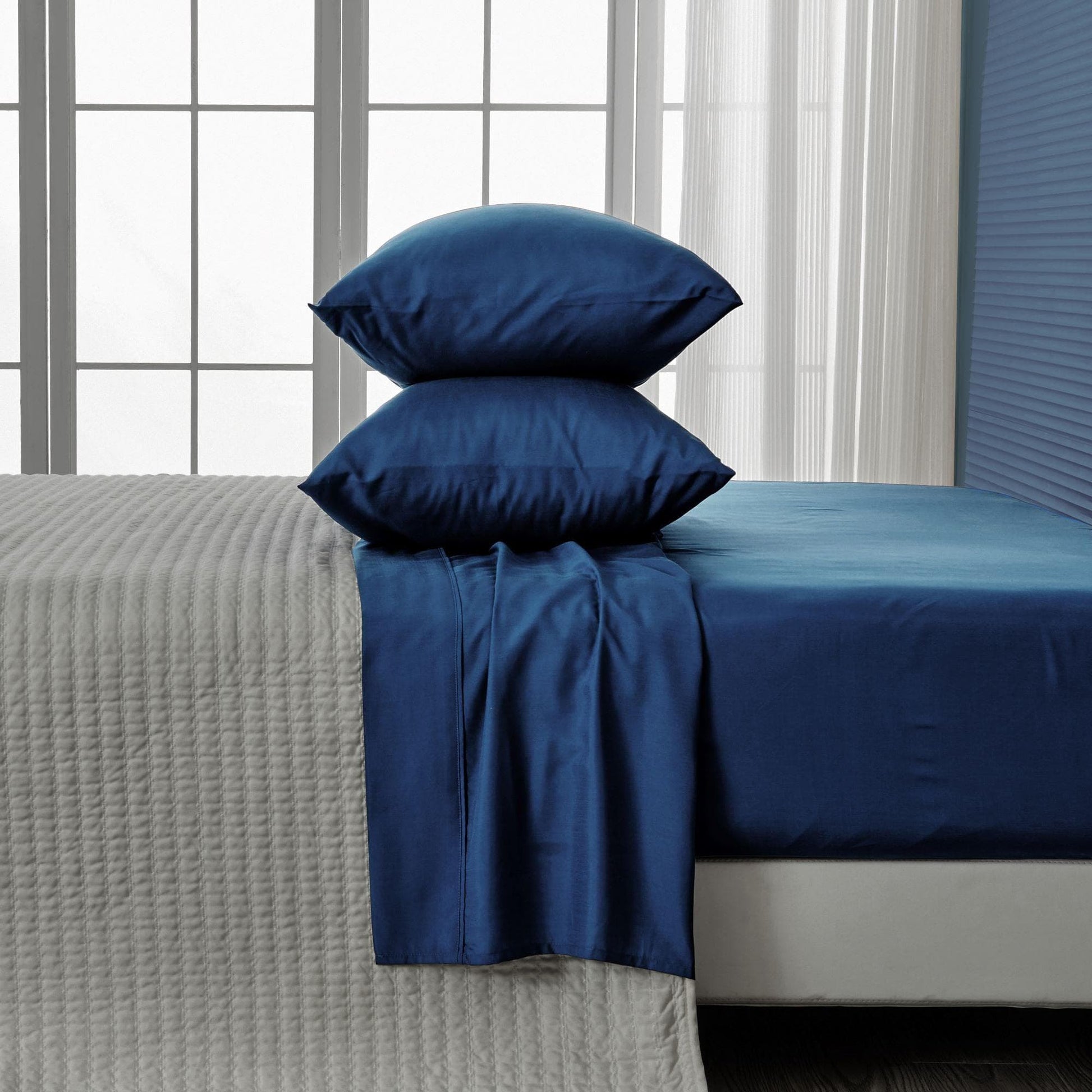 Blue bedding set with pillows on a bed in a room with curtains.