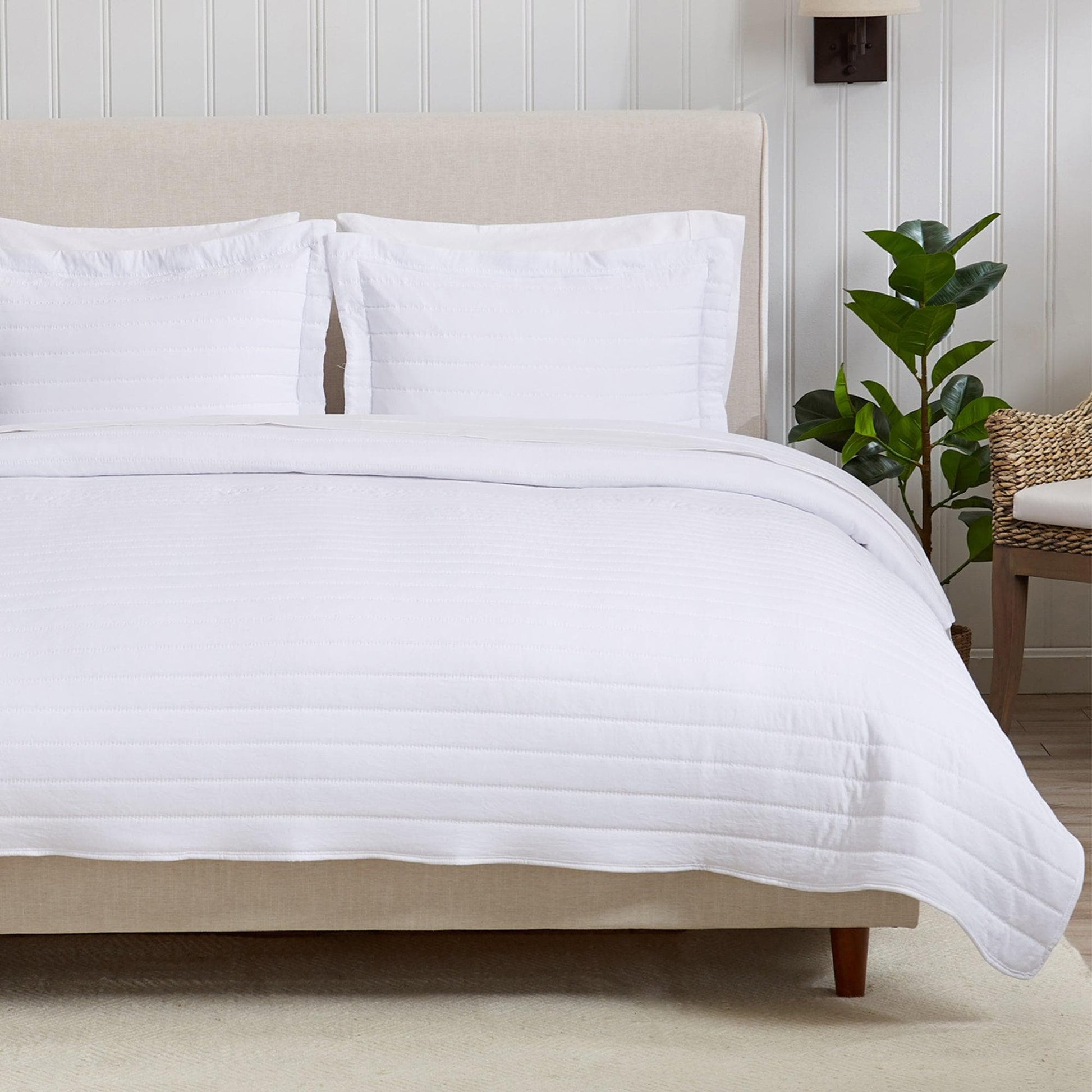 White quilted comforter on a bed with pillows and a plant in the background