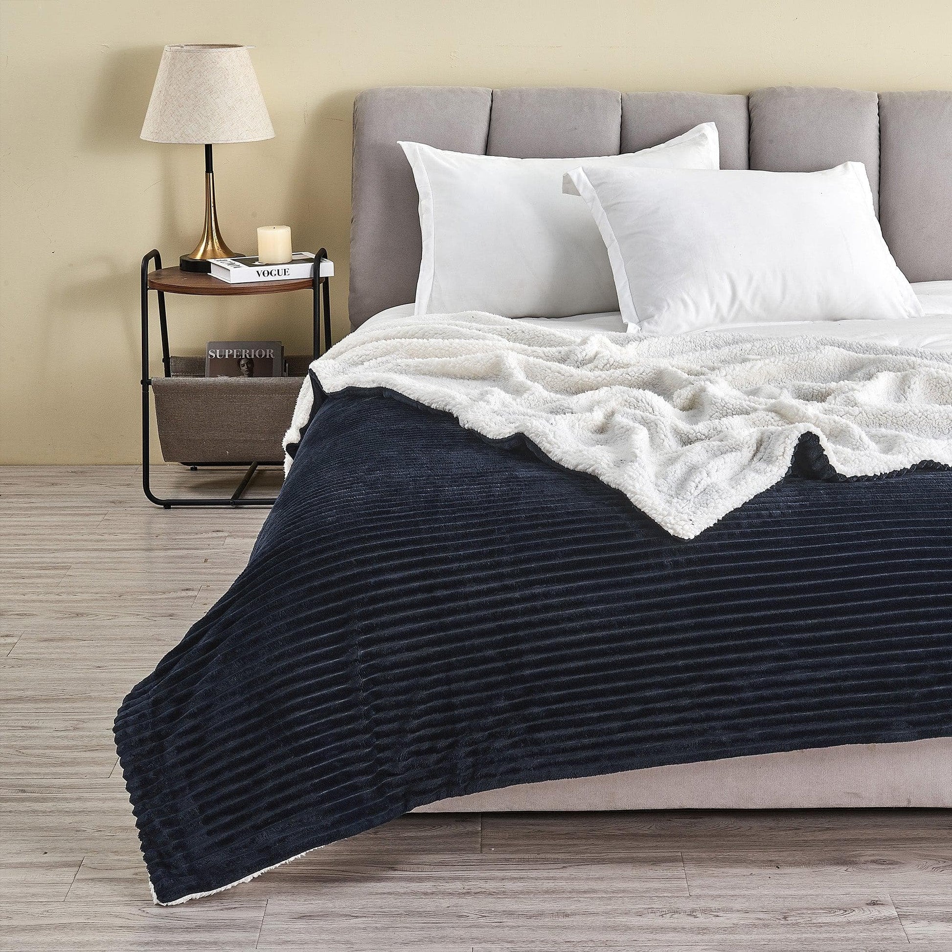 Bedroom with a bed featuring a navy comforter and white pillows, next to a nightstand with a lamp.