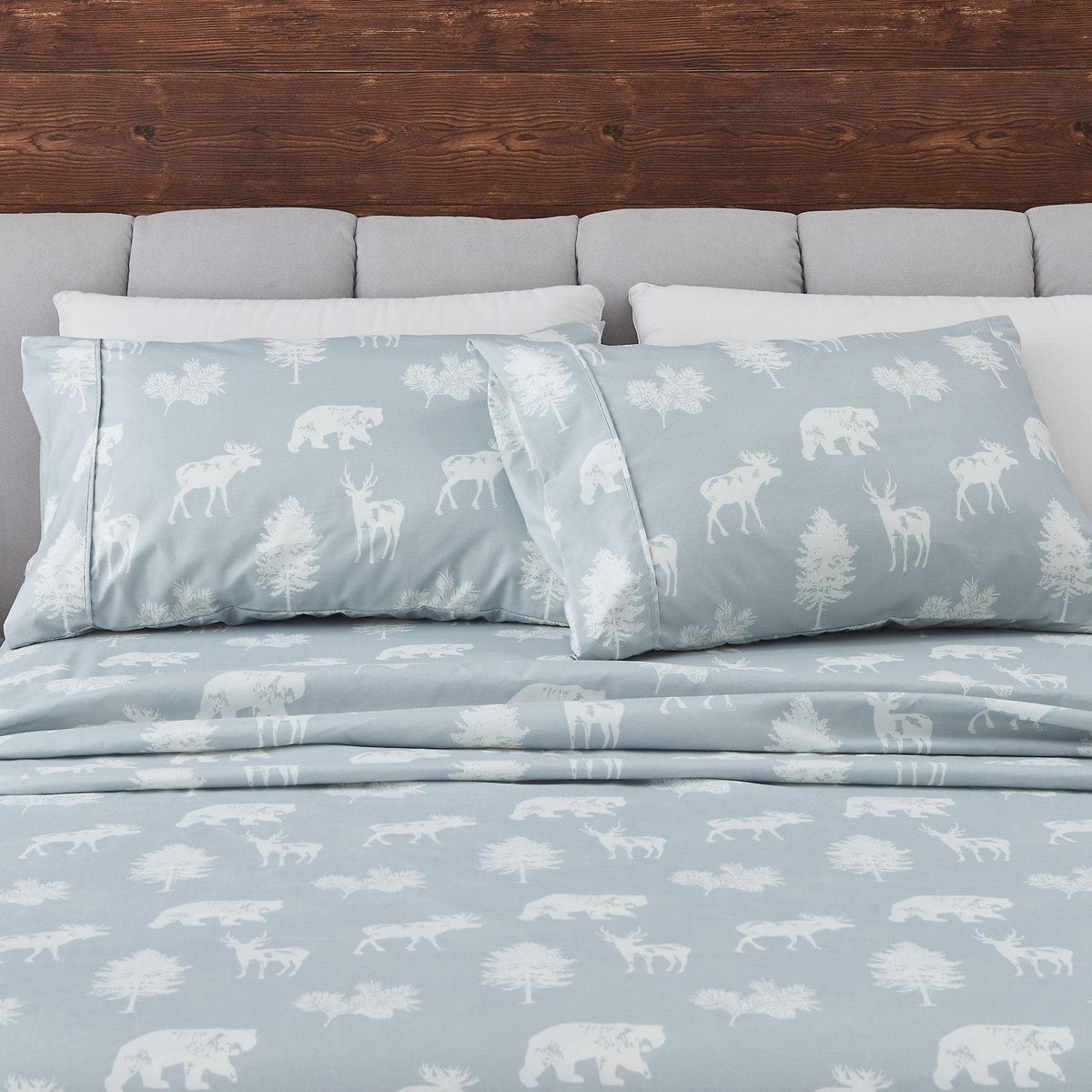 Light blue bedding set with animal patterns on a bed with gray pillows and wooden headboard.