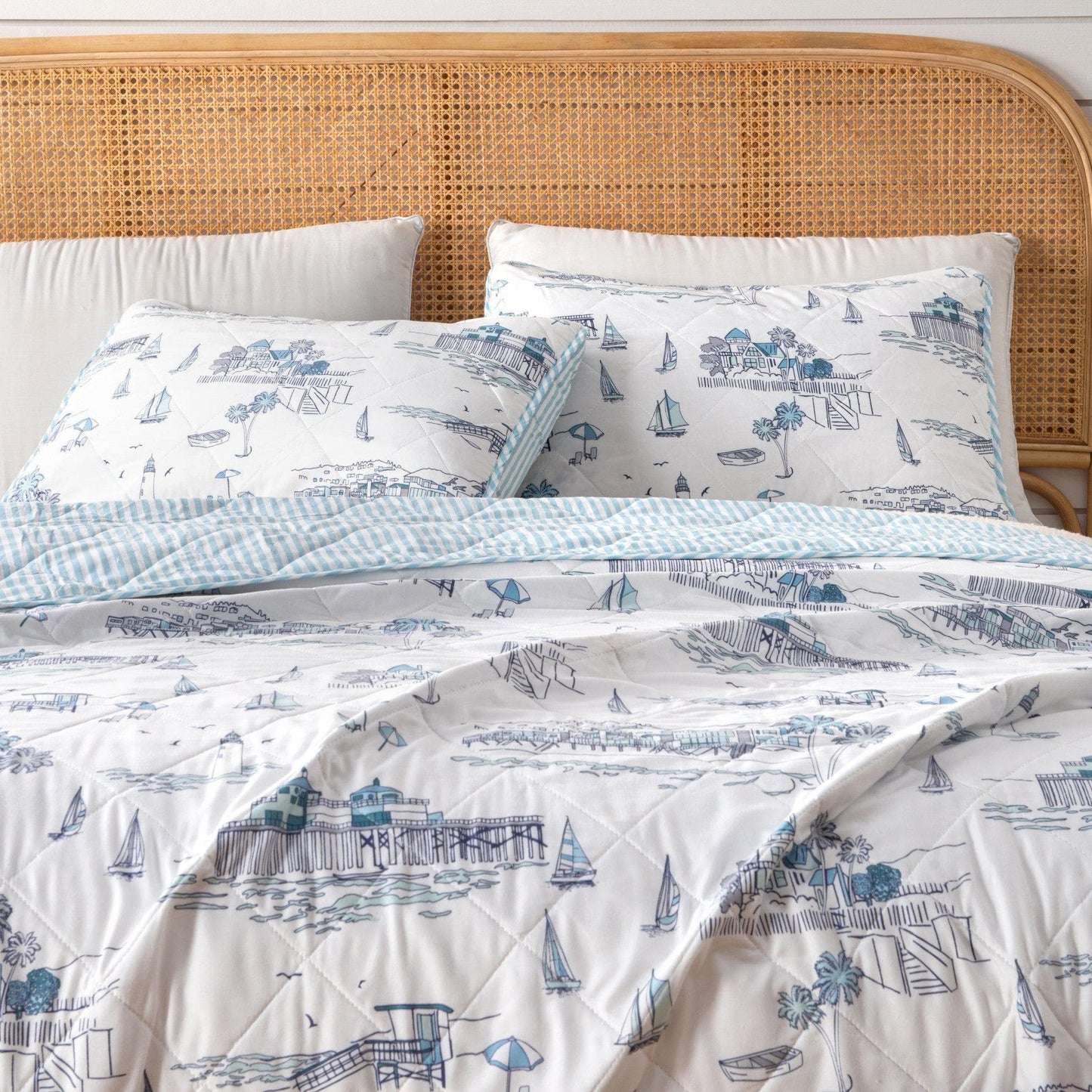 Bed with nautical-themed bedding featuring boats and lighthouses on a white background.