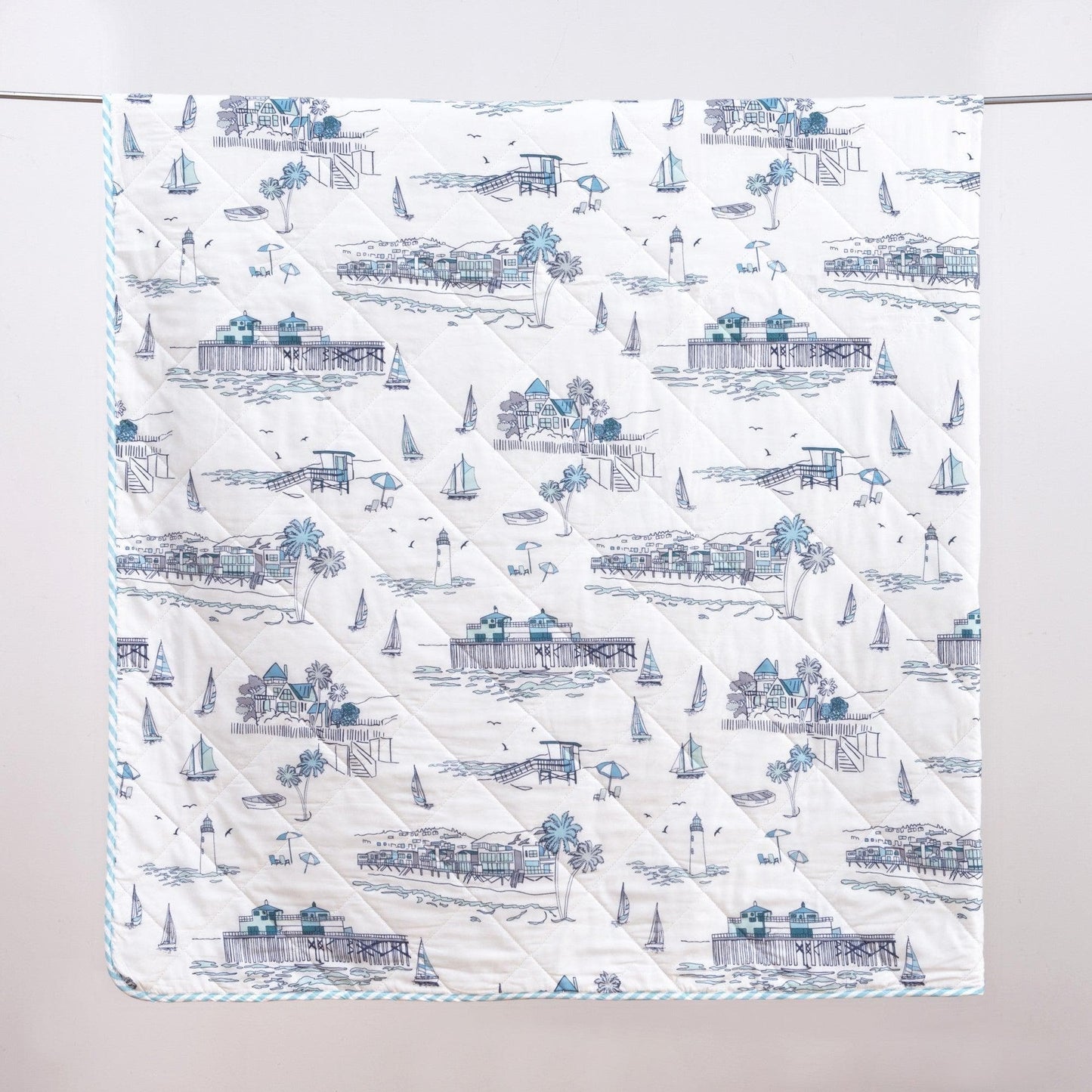 Quilt with coastal pattern featuring houses, boats, and palm trees on a white background