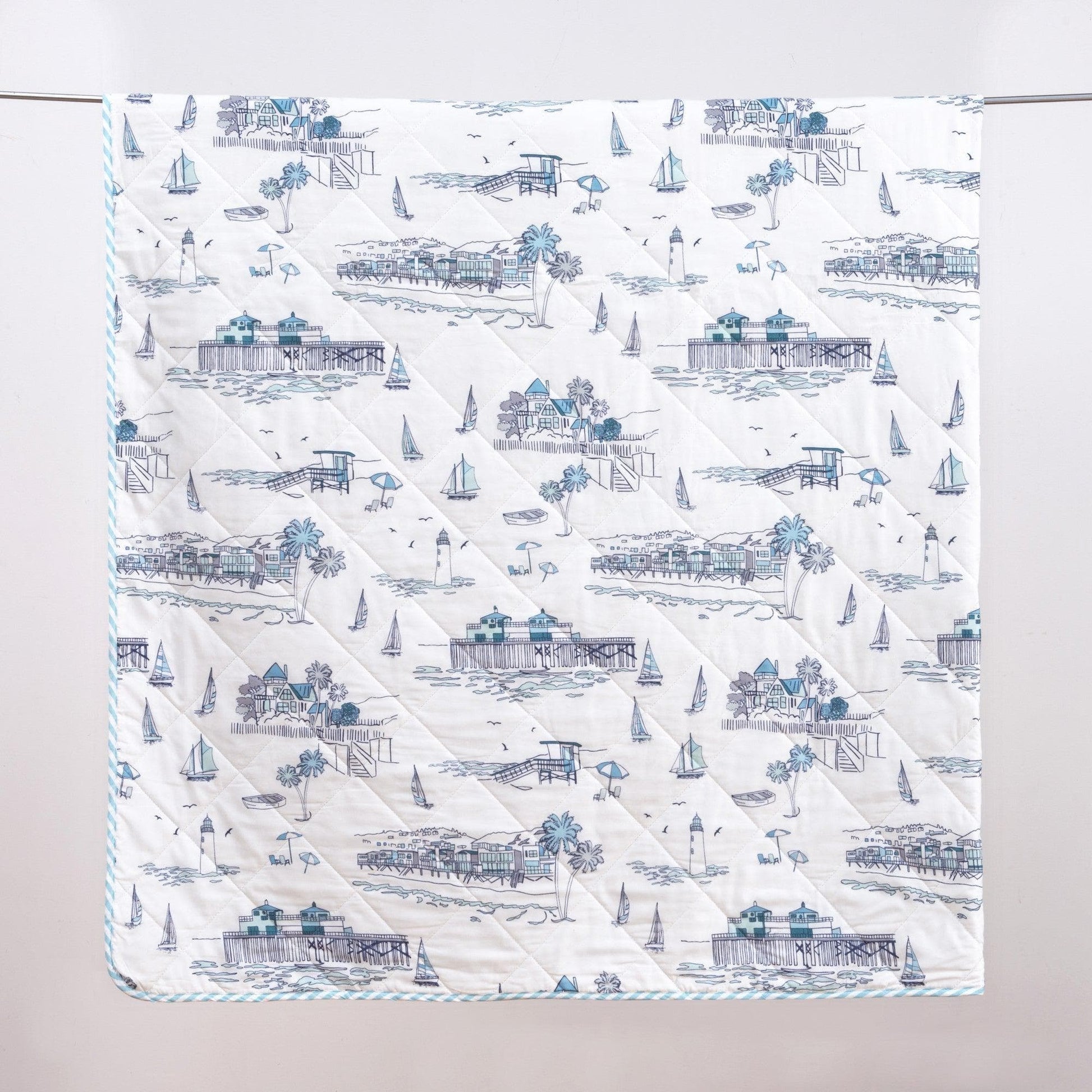 Quilt with coastal pattern featuring houses, boats, and palm trees on a white background