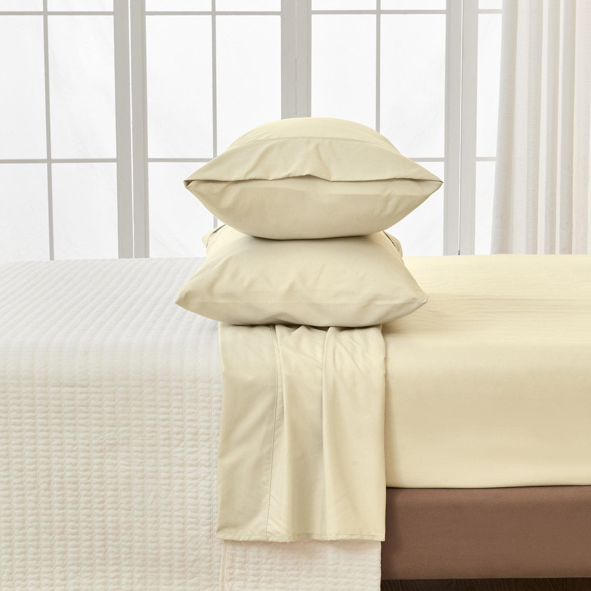 Beige pillows and blanket on a bed with a white window pane background