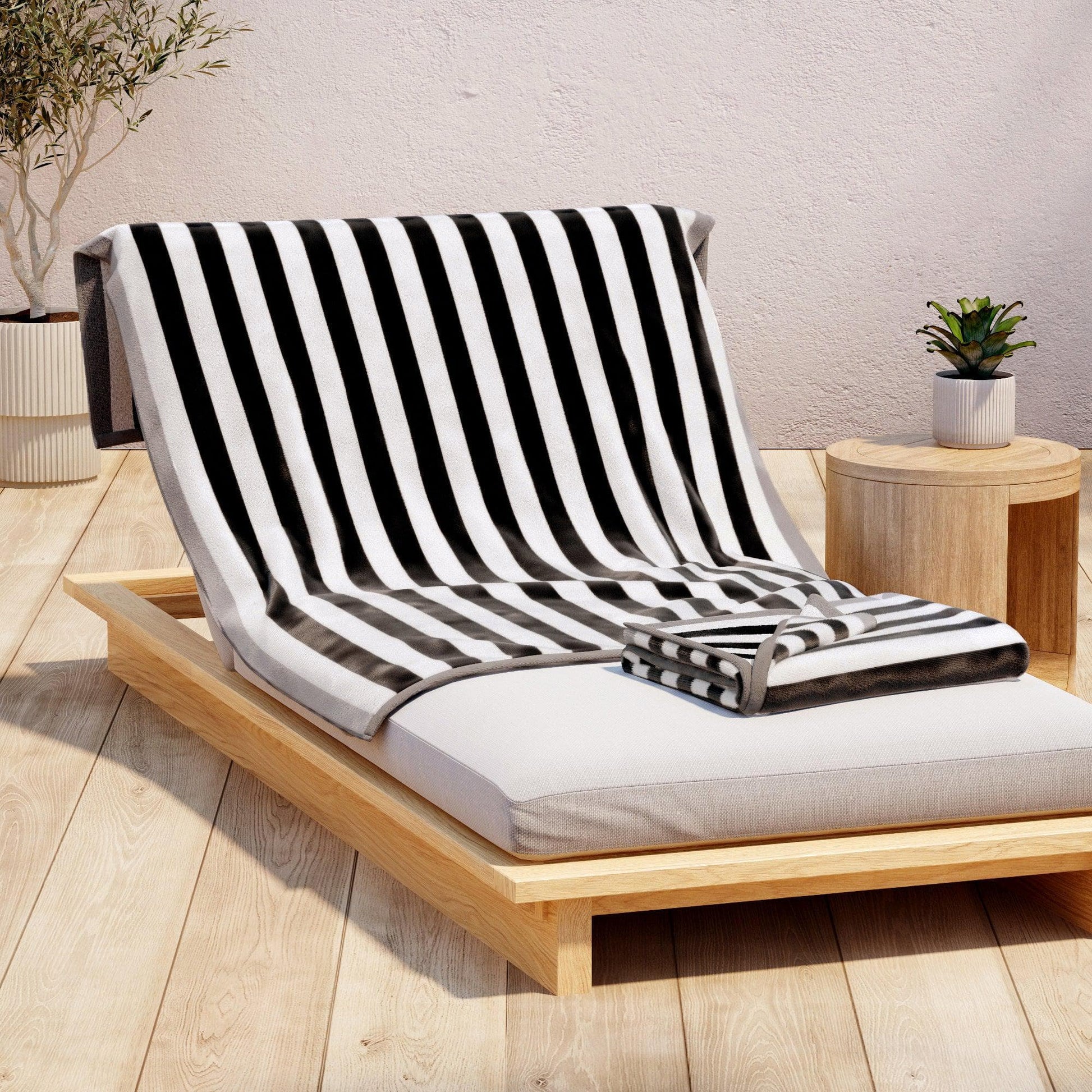 Black and white striped towel draped over a wooden lounge chair with a neutral background