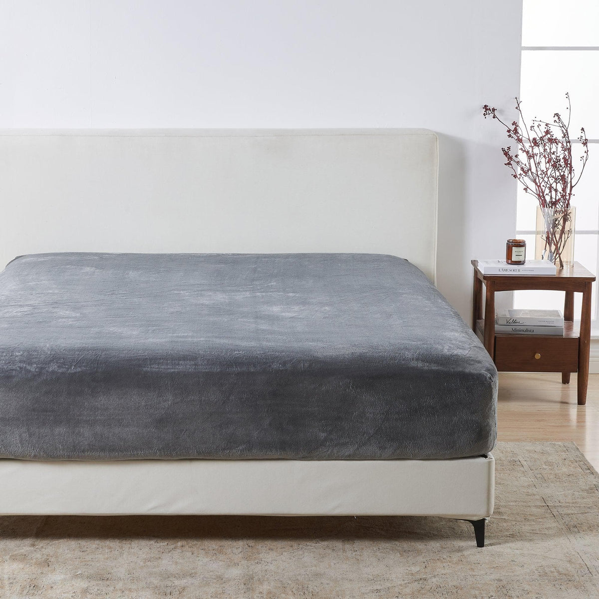 Gray fitted sheet on a bed in a bedroom setting with a side table and decor.