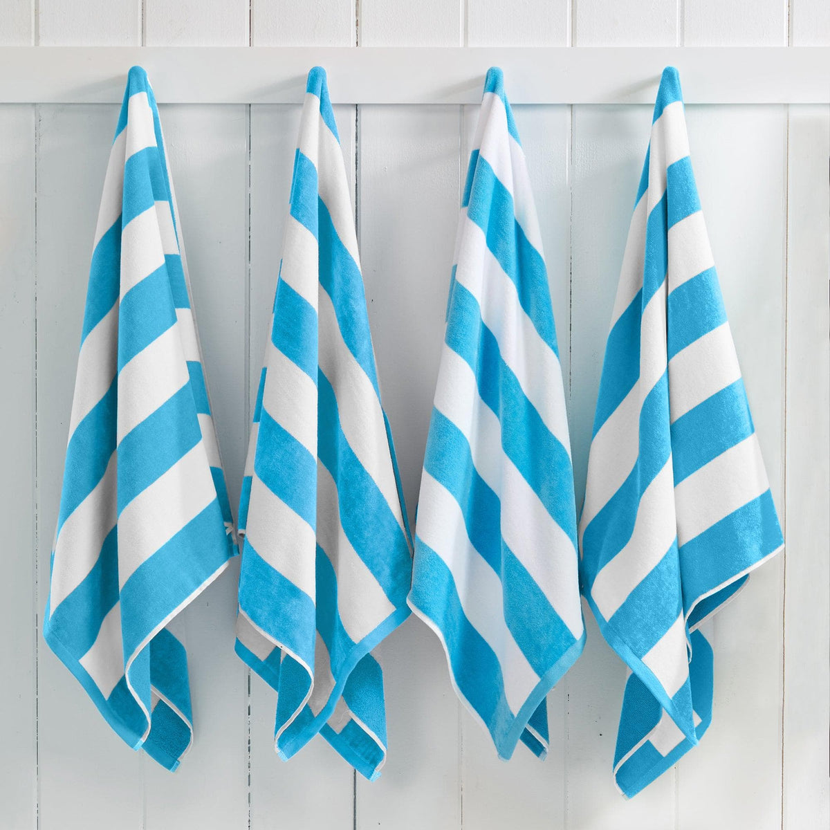 Four blue and white striped towels hanging on a white wooden panel wall.