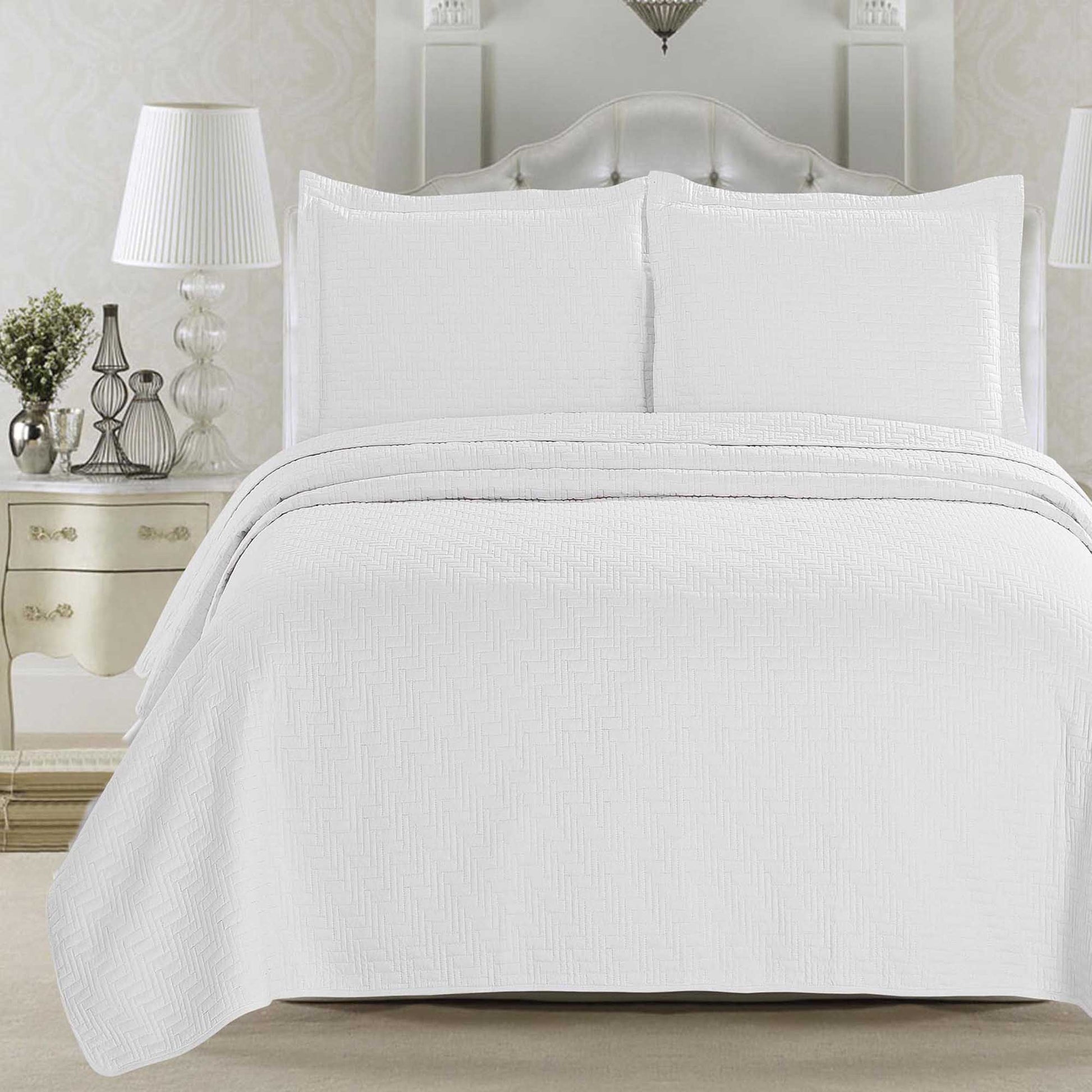 White textured comforter on a bed in a bedroom setting with a nightstand and lamp.