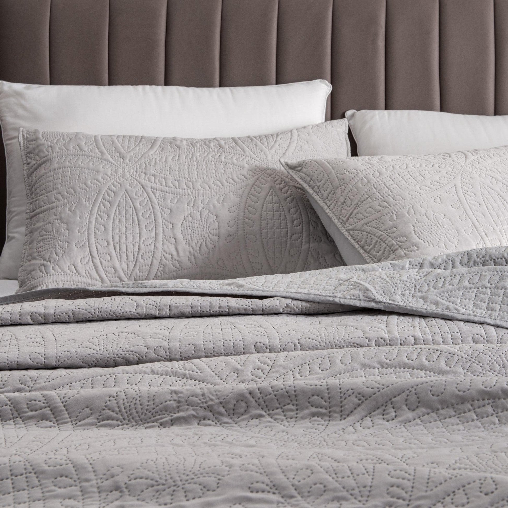 Gray quilted bedding set on a bed with a brown headboard.