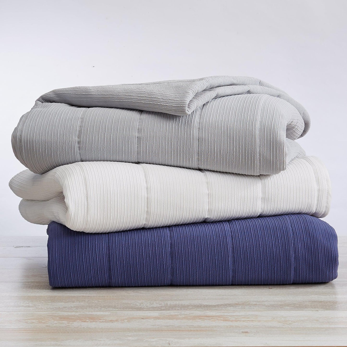 Stack of three folded blankets in gray, white, and blue on a light wooden surface.