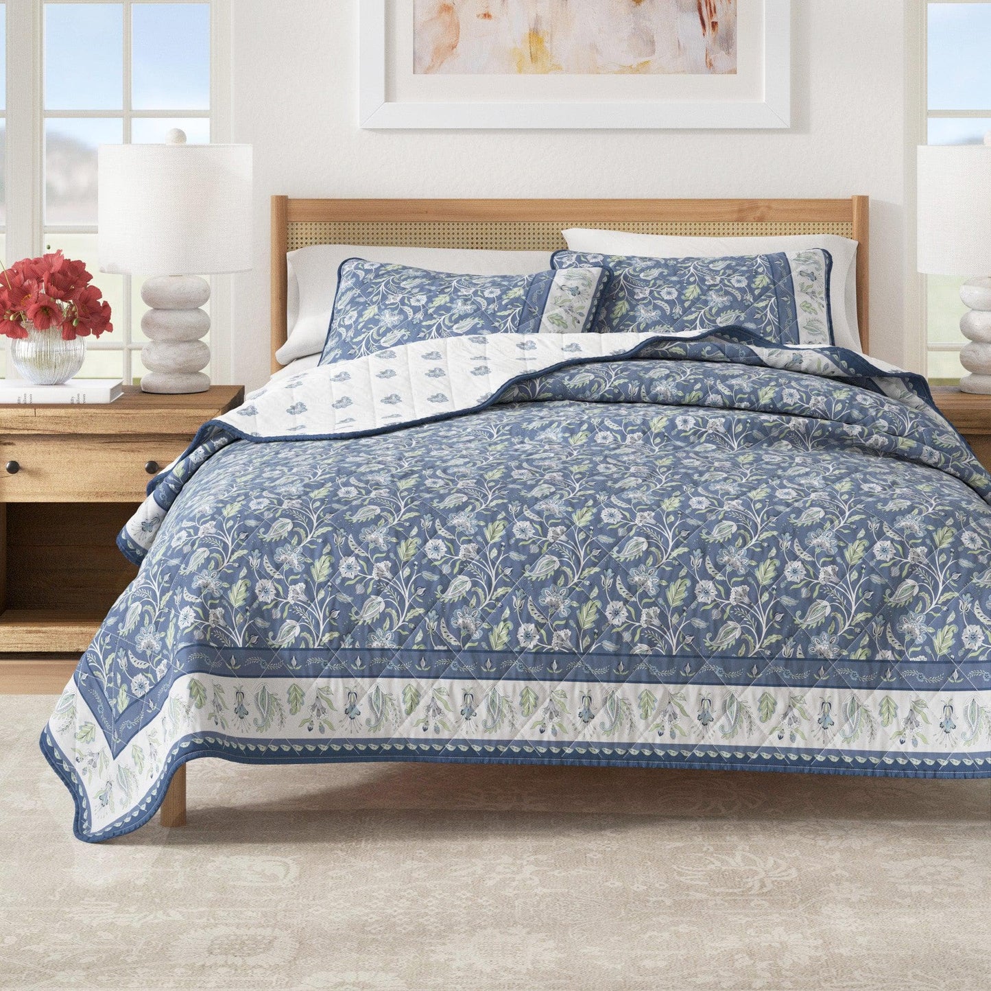 Bedroom with a bed covered in blue floral bedding, wooden headboard, and side table with lamp.