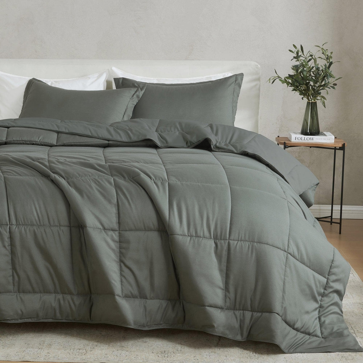 Gray comforter set on a bed with pillows and a side table in the background.
