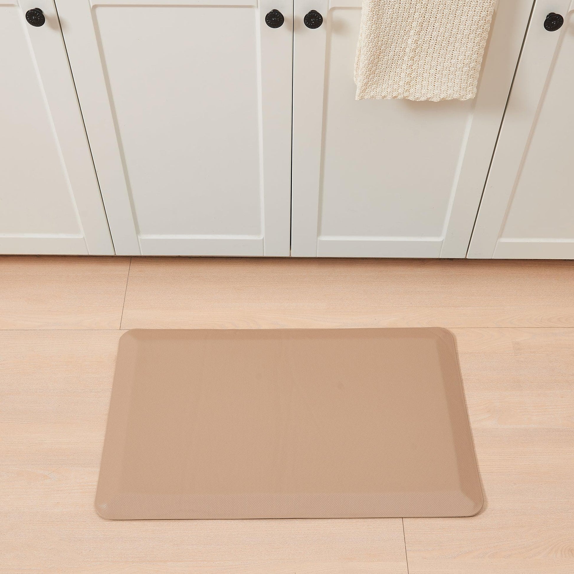 Beige mat on a wooden floor in front of white cabinets.