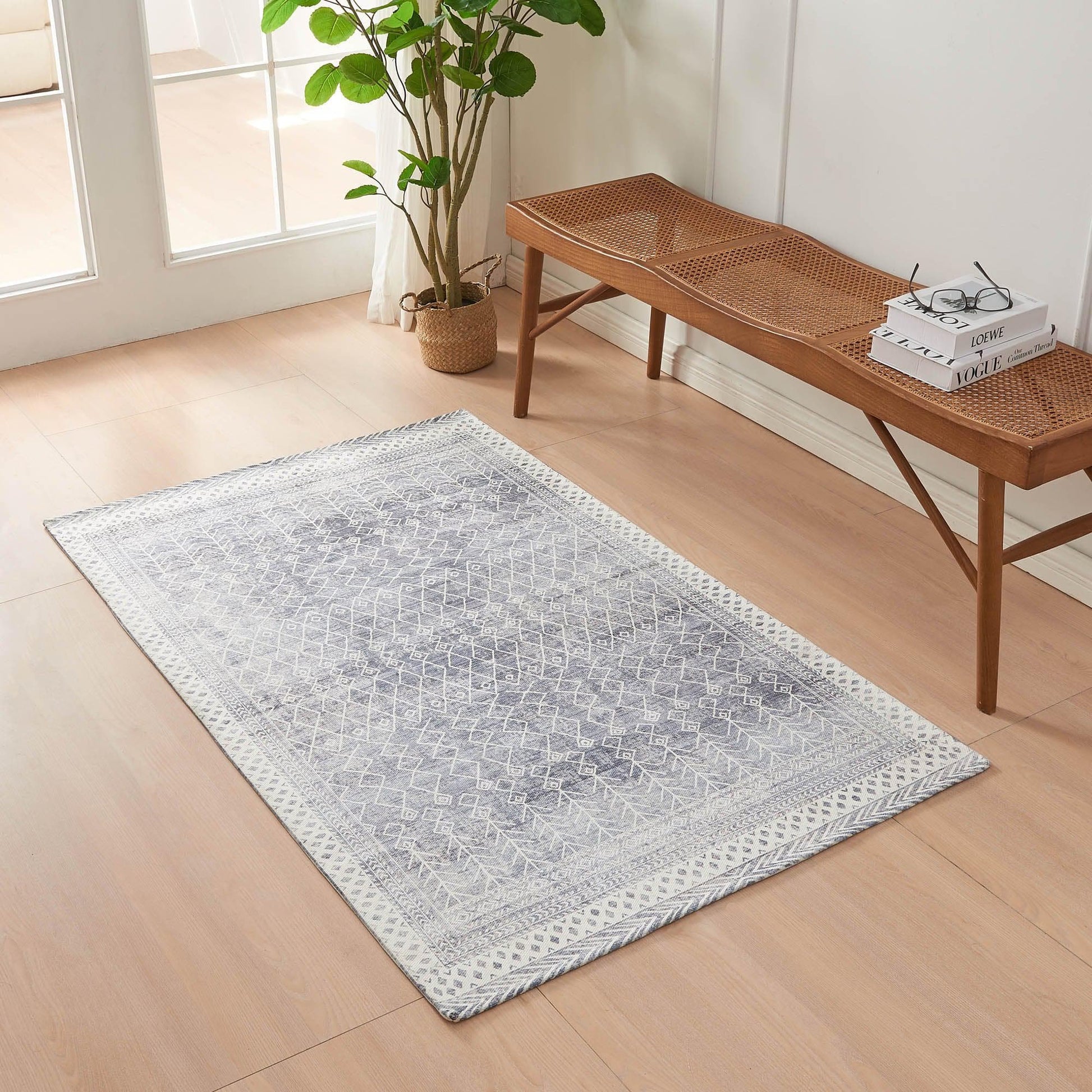 Gray patterned rug on a wooden floor with a wooden bench and plant in the background.