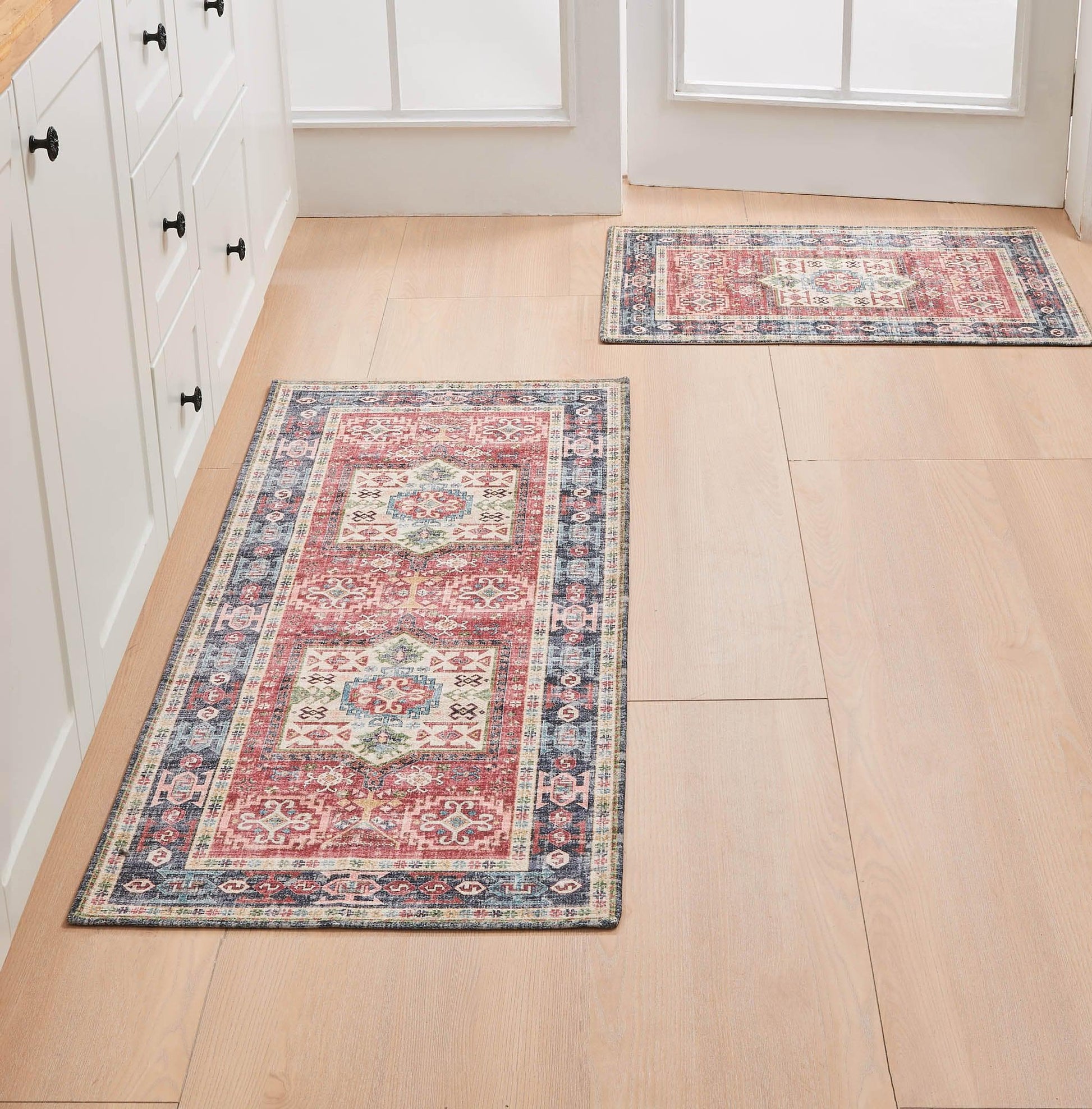 Two patterned rugs on a wooden floor in a room with white cabinets.