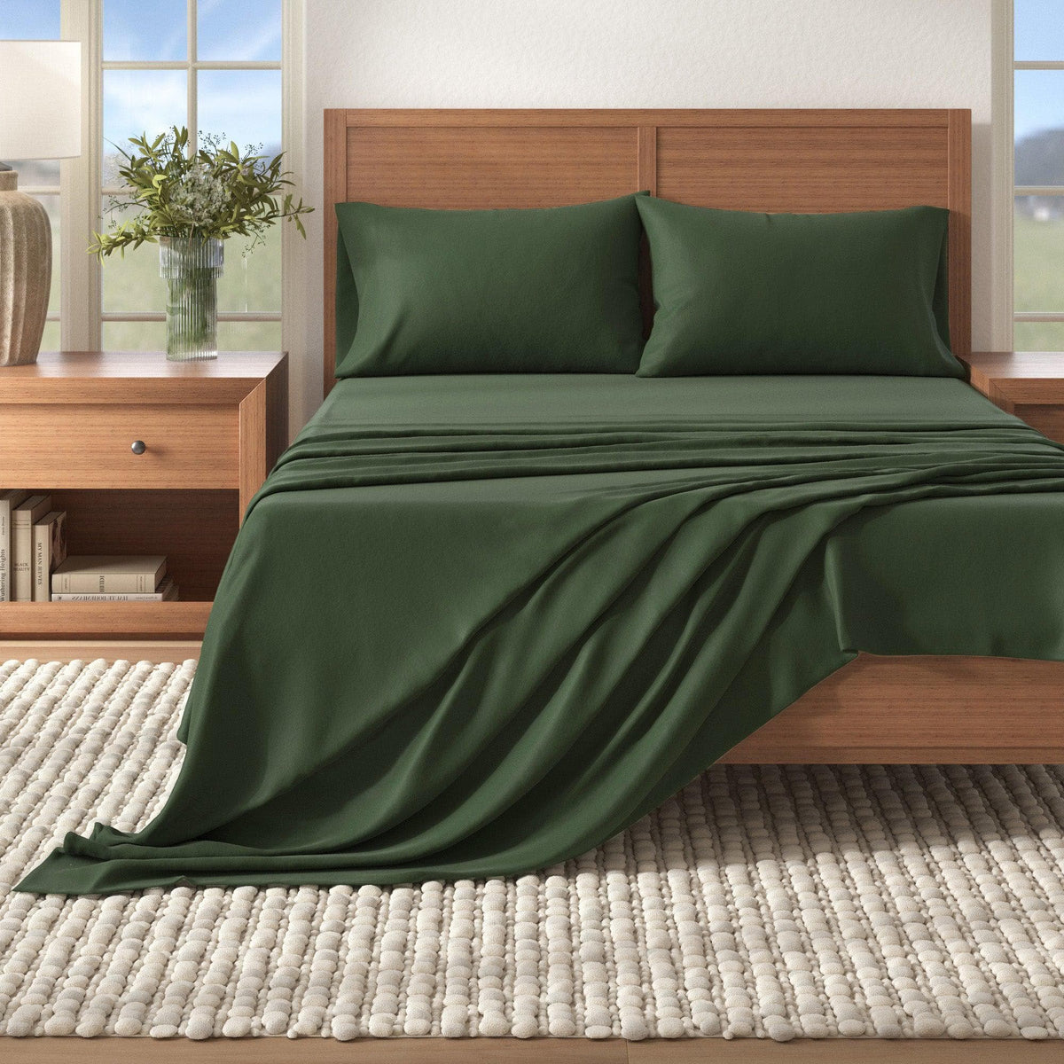 Green bedspread on a wooden bed in a bedroom setting with a window and vase in the background.