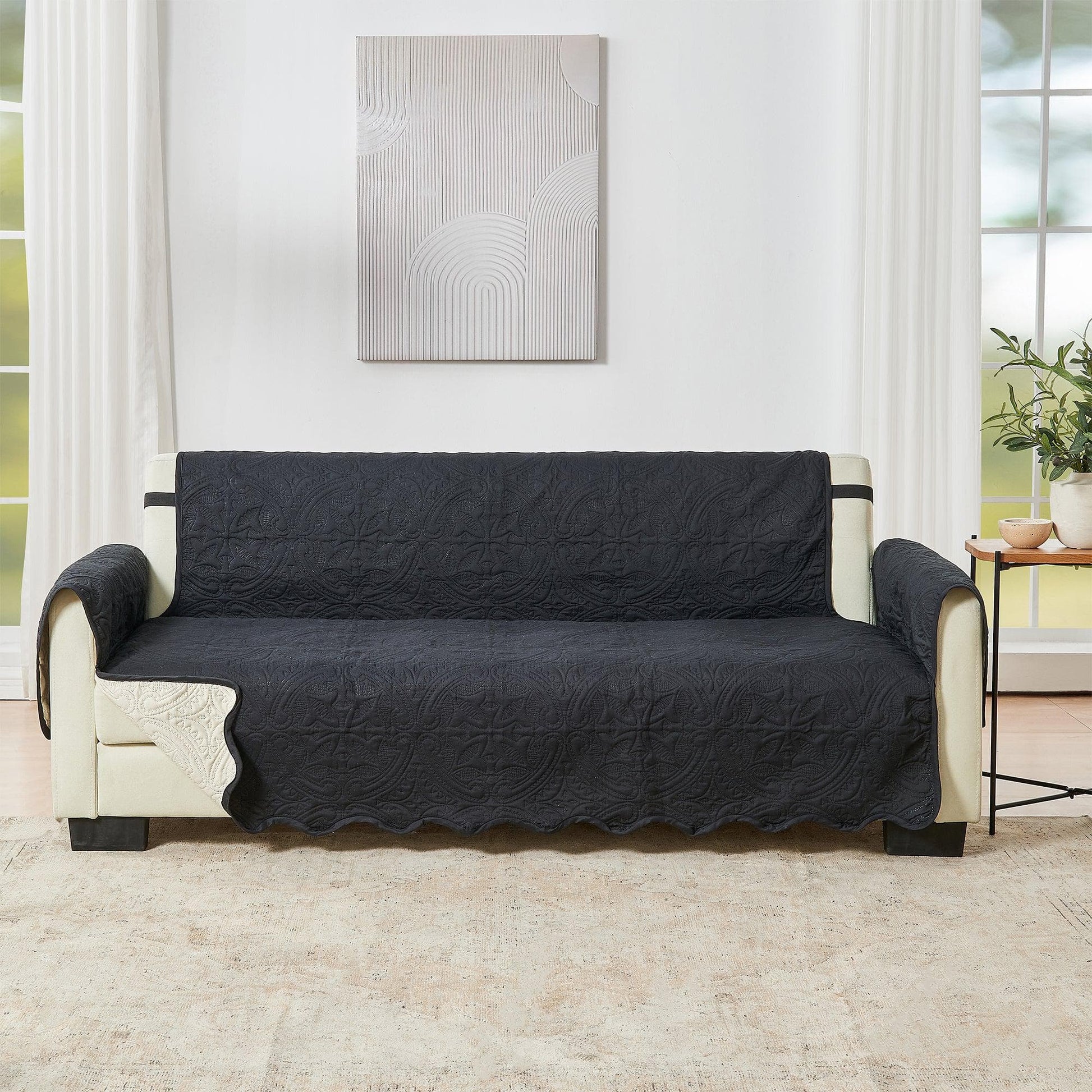 Black sofa cover on a beige sofa in a living room setting with a painting on the wall.