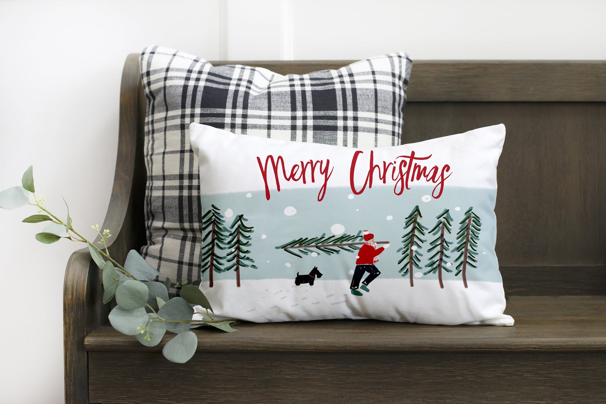 Merry Christmas with Man Carrying Tree 12x20 inch Pillow Cover on a cozy bench with plaid pillows.