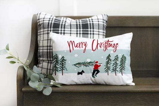 Merry Christmas with Man Carrying Tree 12x20 inch Pillow Cover on a cozy bench with plaid pillows.