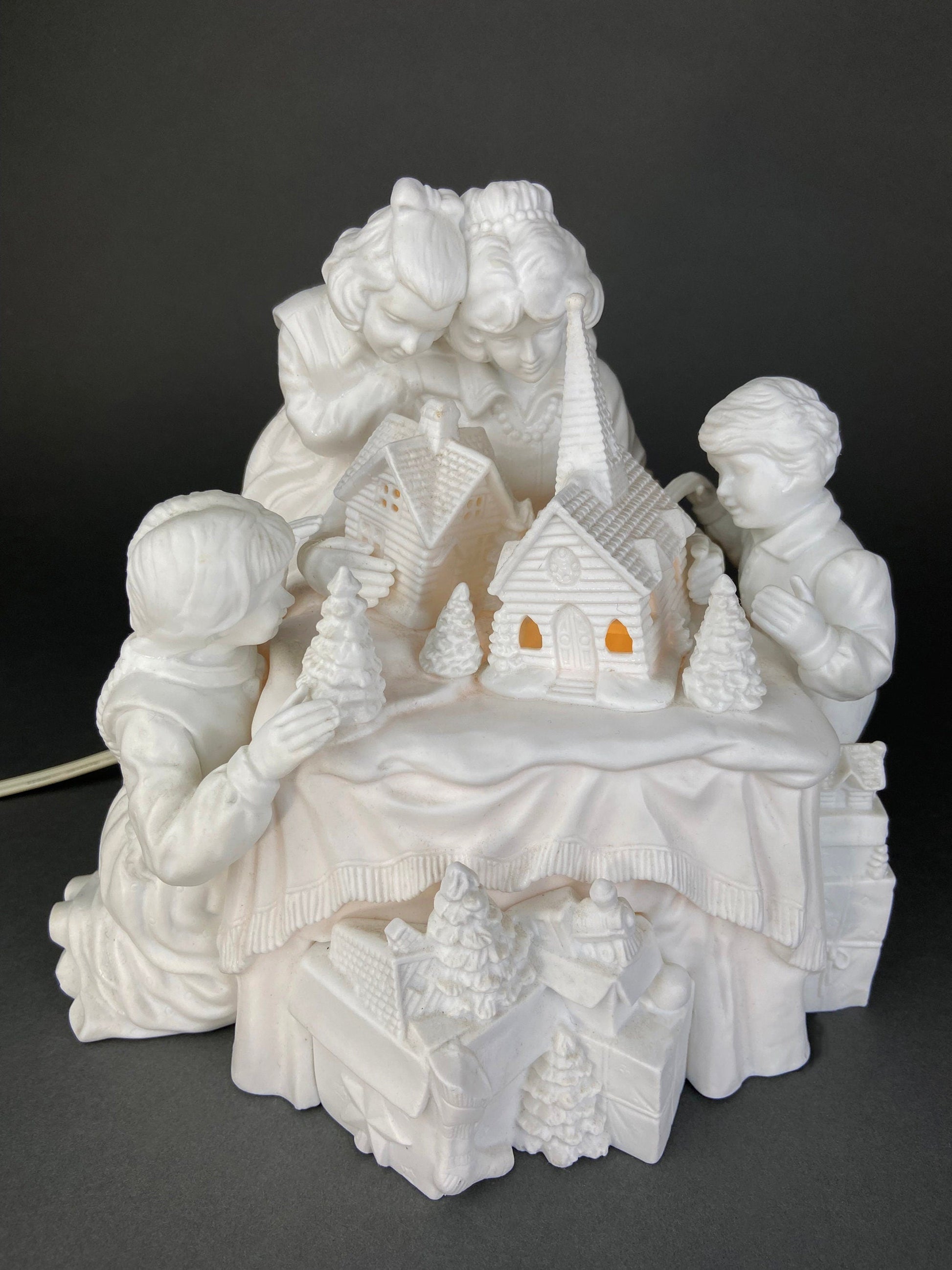 White ceramic nativity scene with two children and a church on a dark background