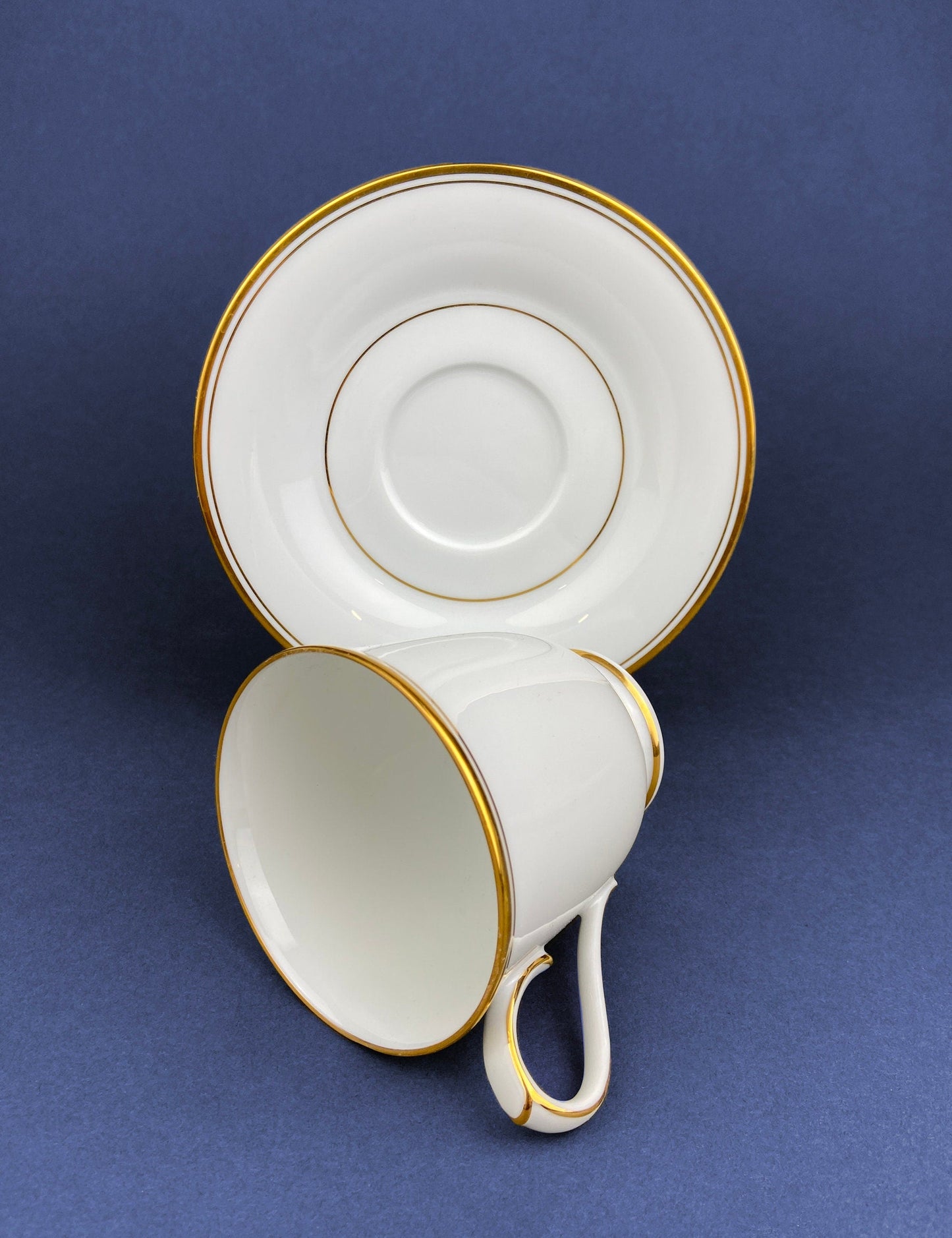 White teacup and saucer with gold trim on a blue background