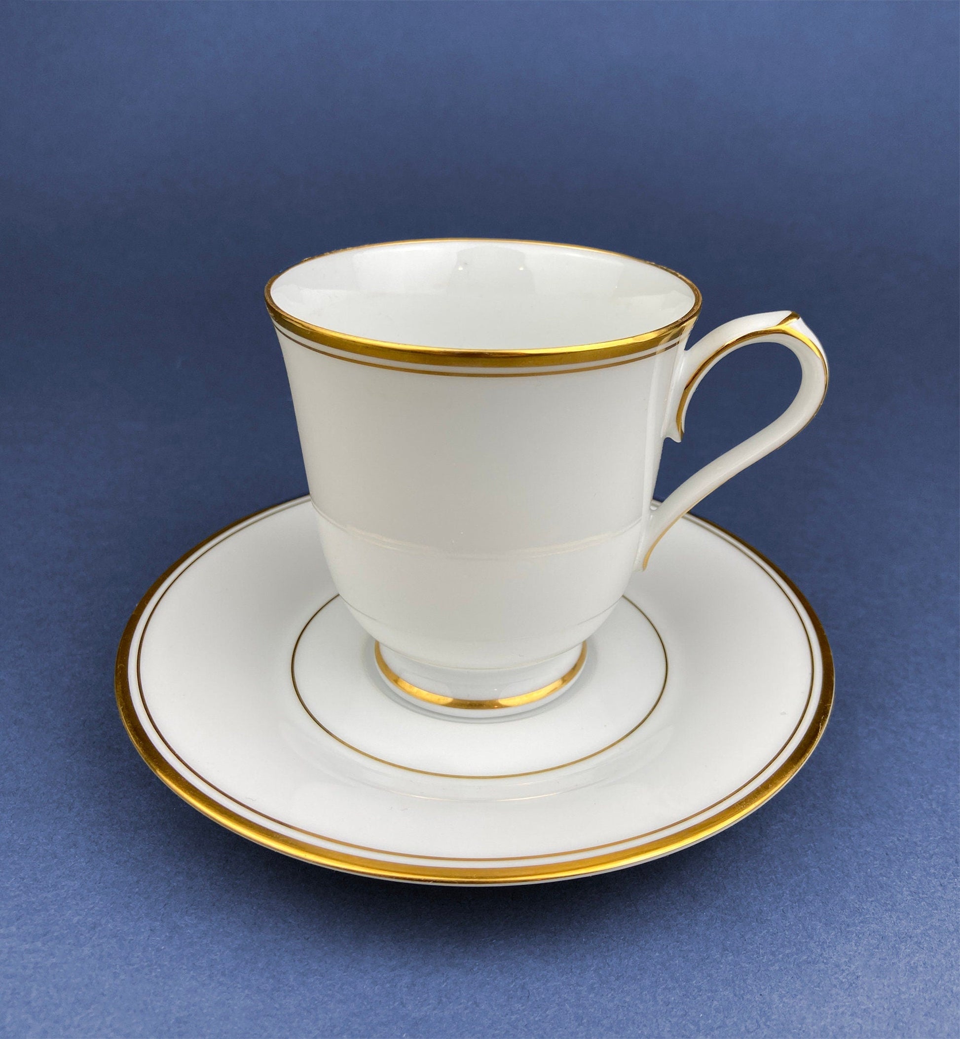 White teacup with gold trim on a matching saucer against a blue background