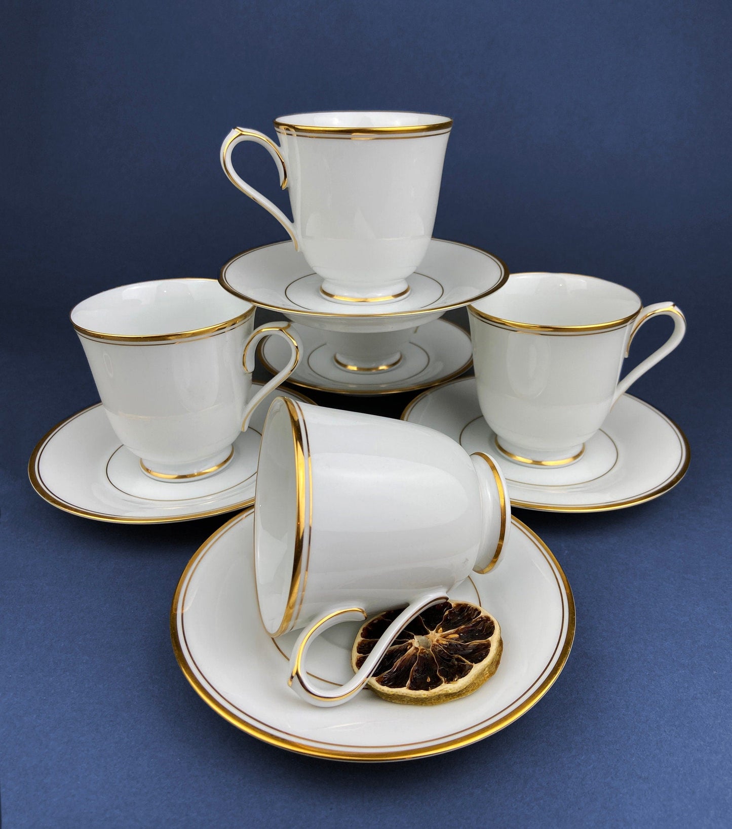 Set of white tea cups and saucers with gold trim on a blue background