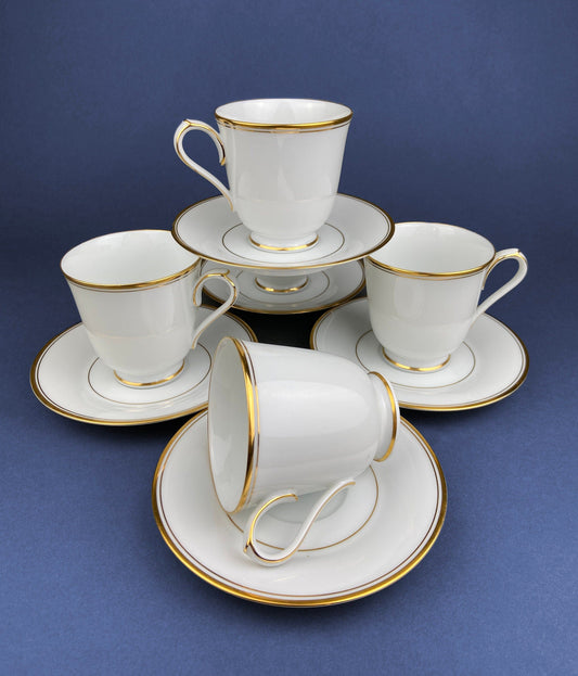 Set of white tea cups and saucers with gold trim on a blue background