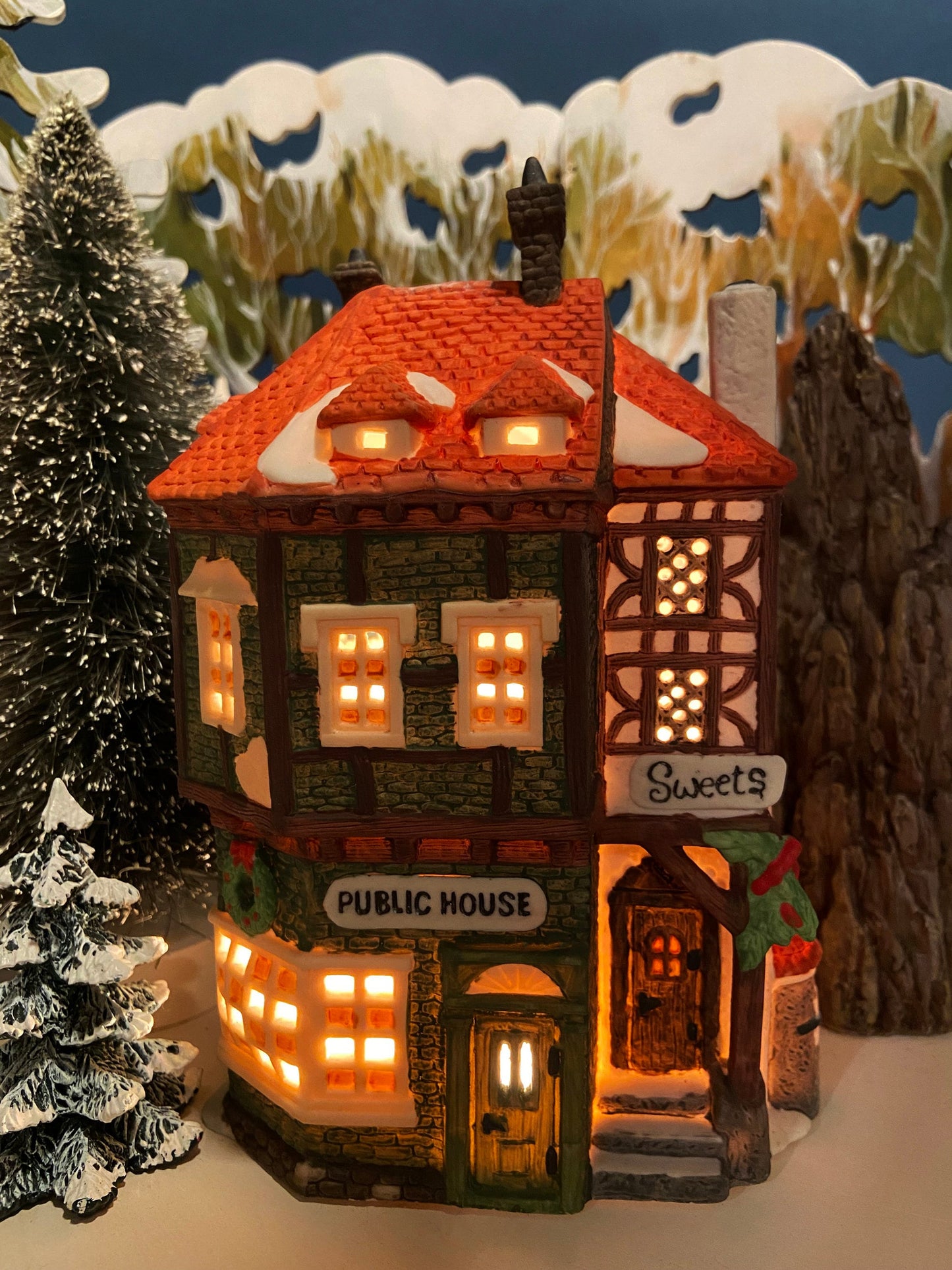 Decorative model of a Public House with lit windows, surrounded by snowy trees and landscape.